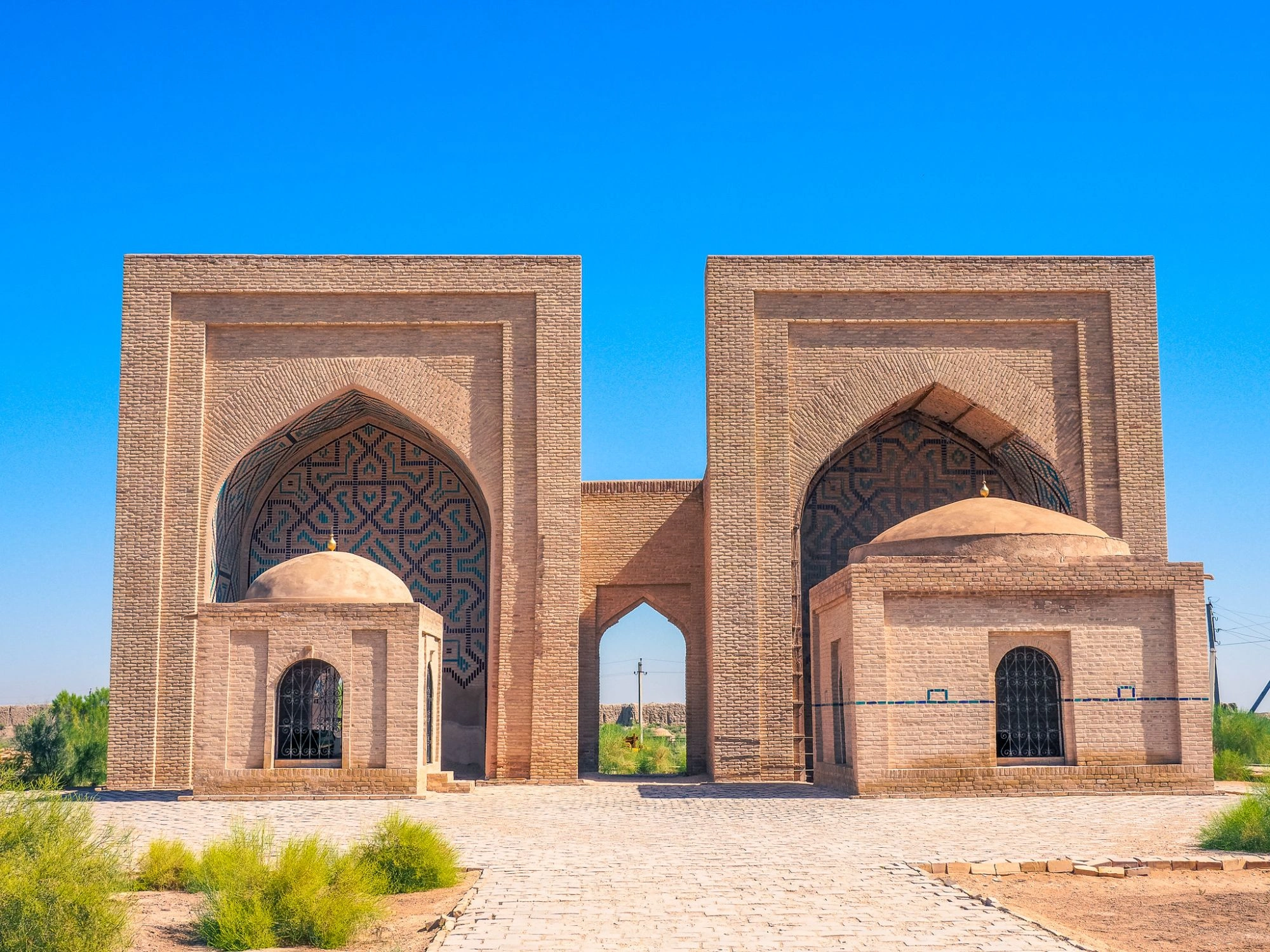 Historic mosque and arched gateway in Merv, Turkmenistan, with tilework under clear skies.