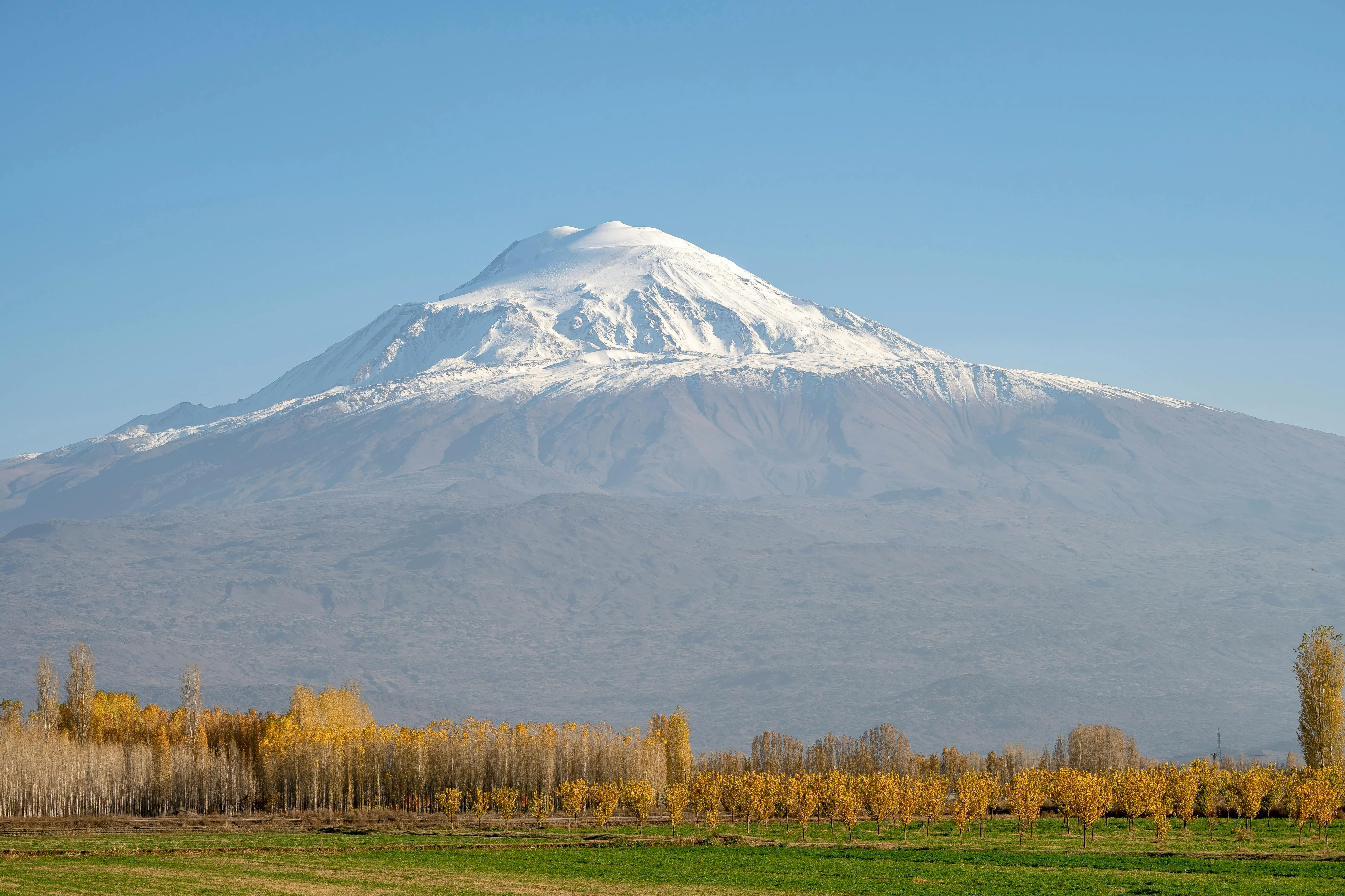 Mount Ararat’s snow-capped peak rising above autumn-colored trees. Blue skies and sun is shining.
