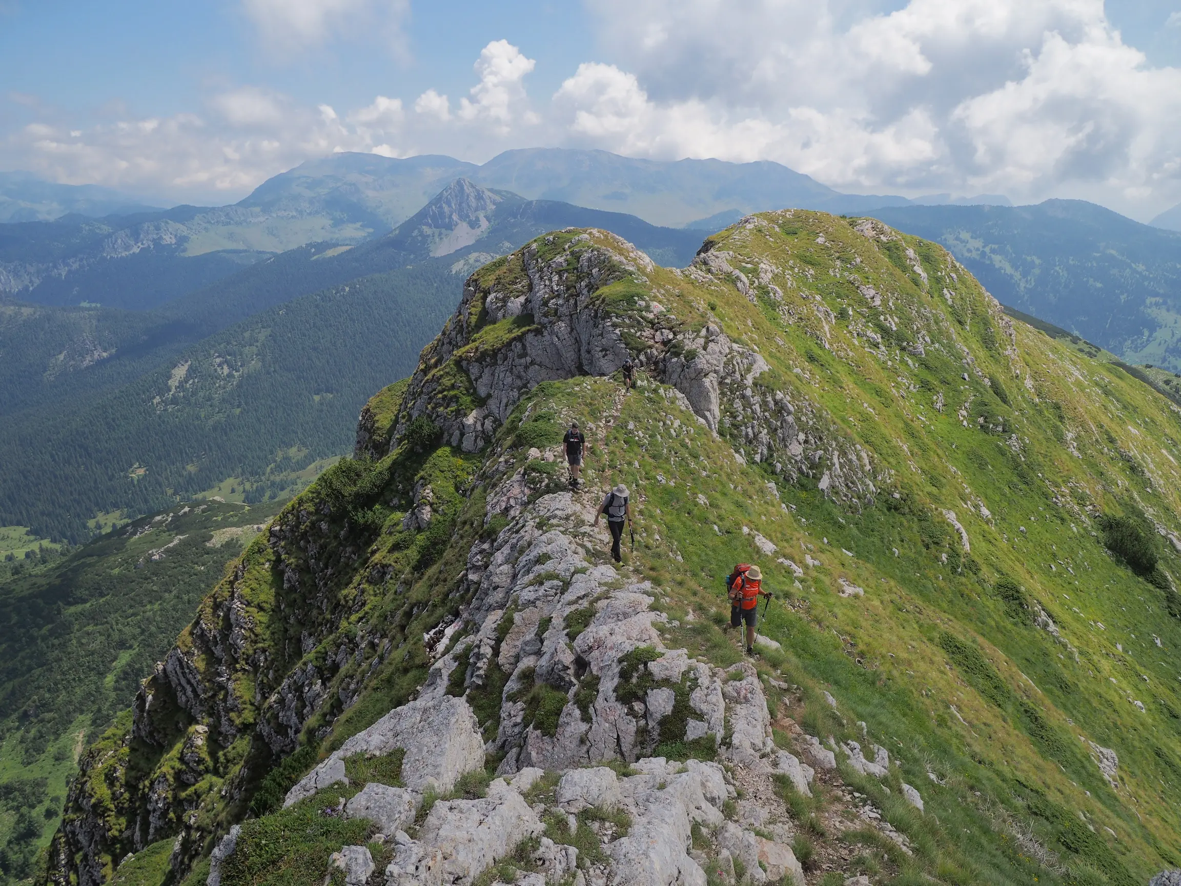 Three hikers traverse the narrow rocky Hajla Ridge with sweeping mountain views stretching into the distance.