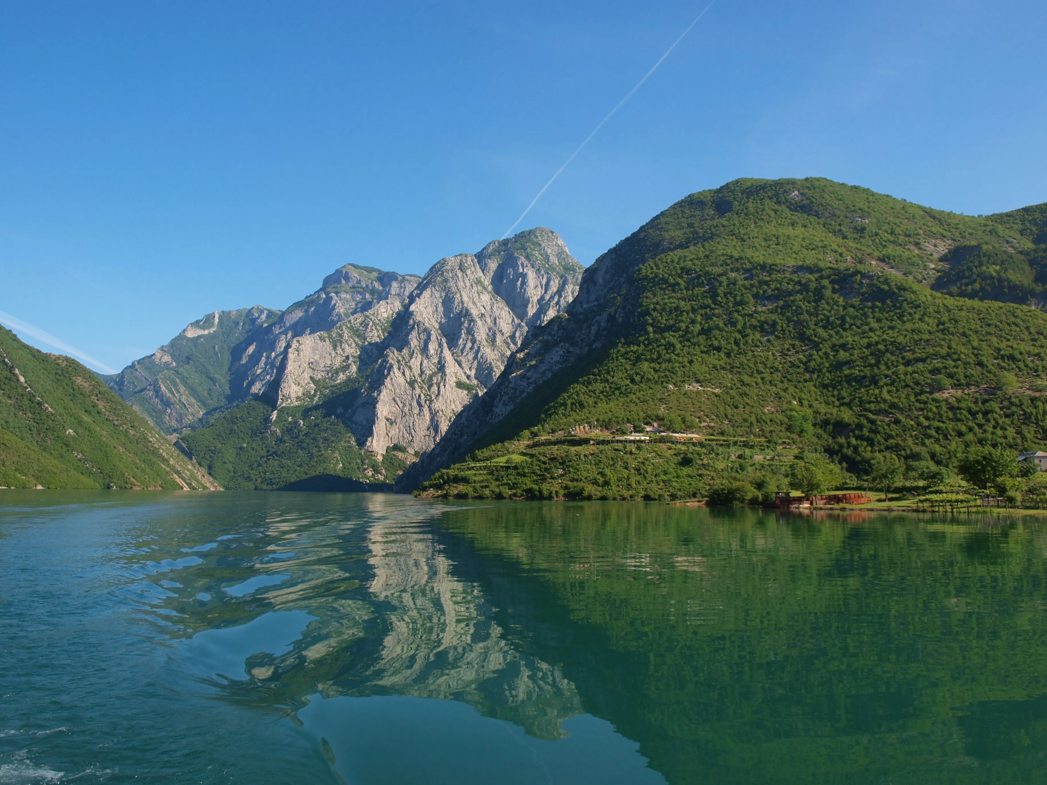 The emerald waters of Koman Lake reflecting the surrounding mountains, a stunning view from a boat journey in Albania.