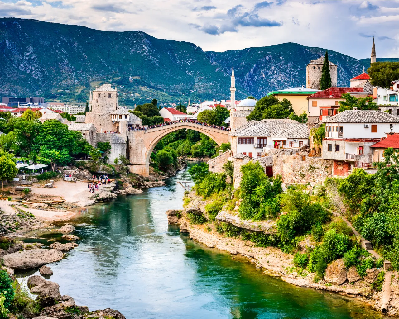 Mostar, Bosnia - The historic Stari Most bridge spans the Neretva River, stone buildings and lush greenery around it.