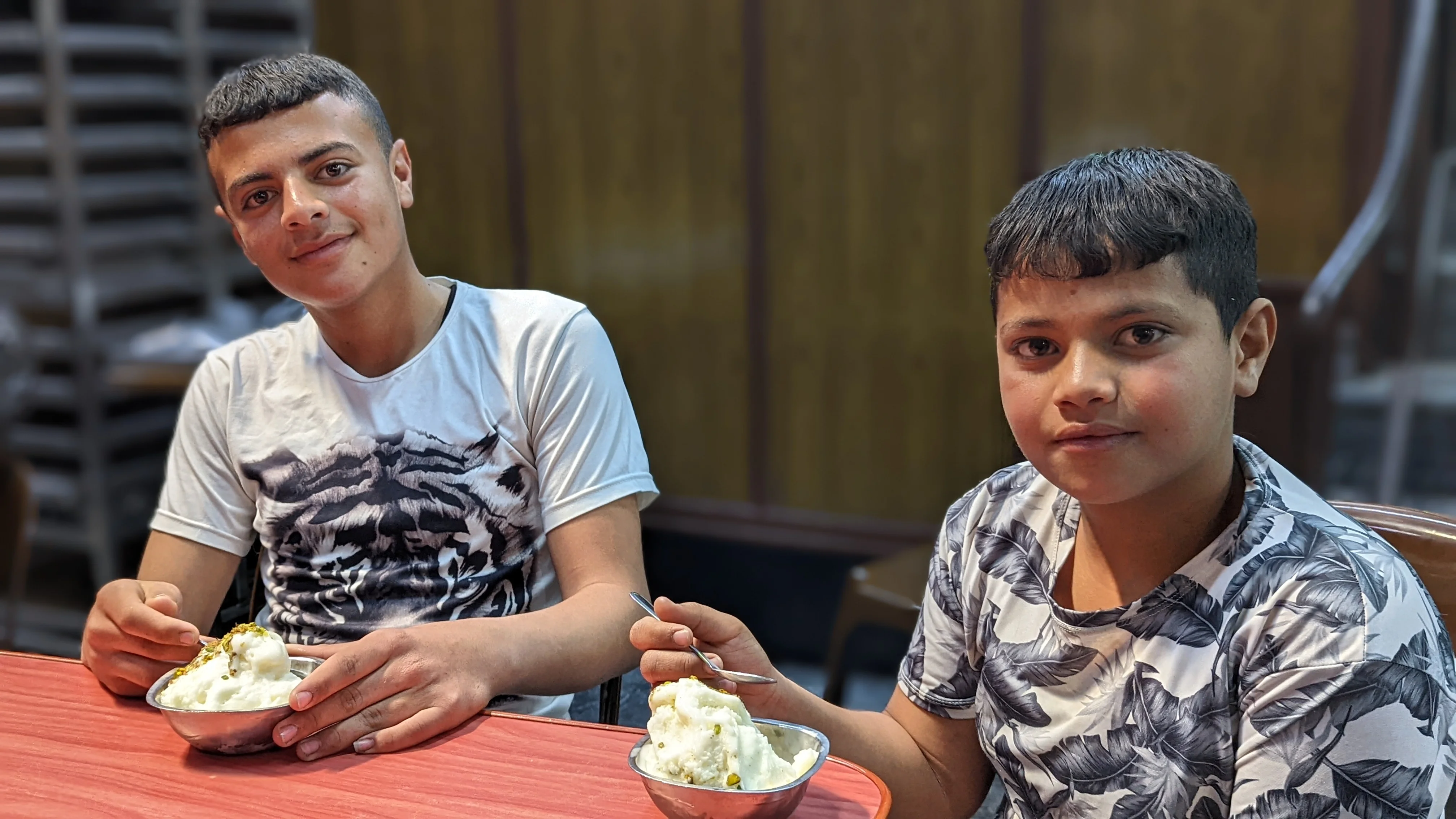 Two boys smiling while enjoying Syrian mastic ice cream topped with crushed pistachios