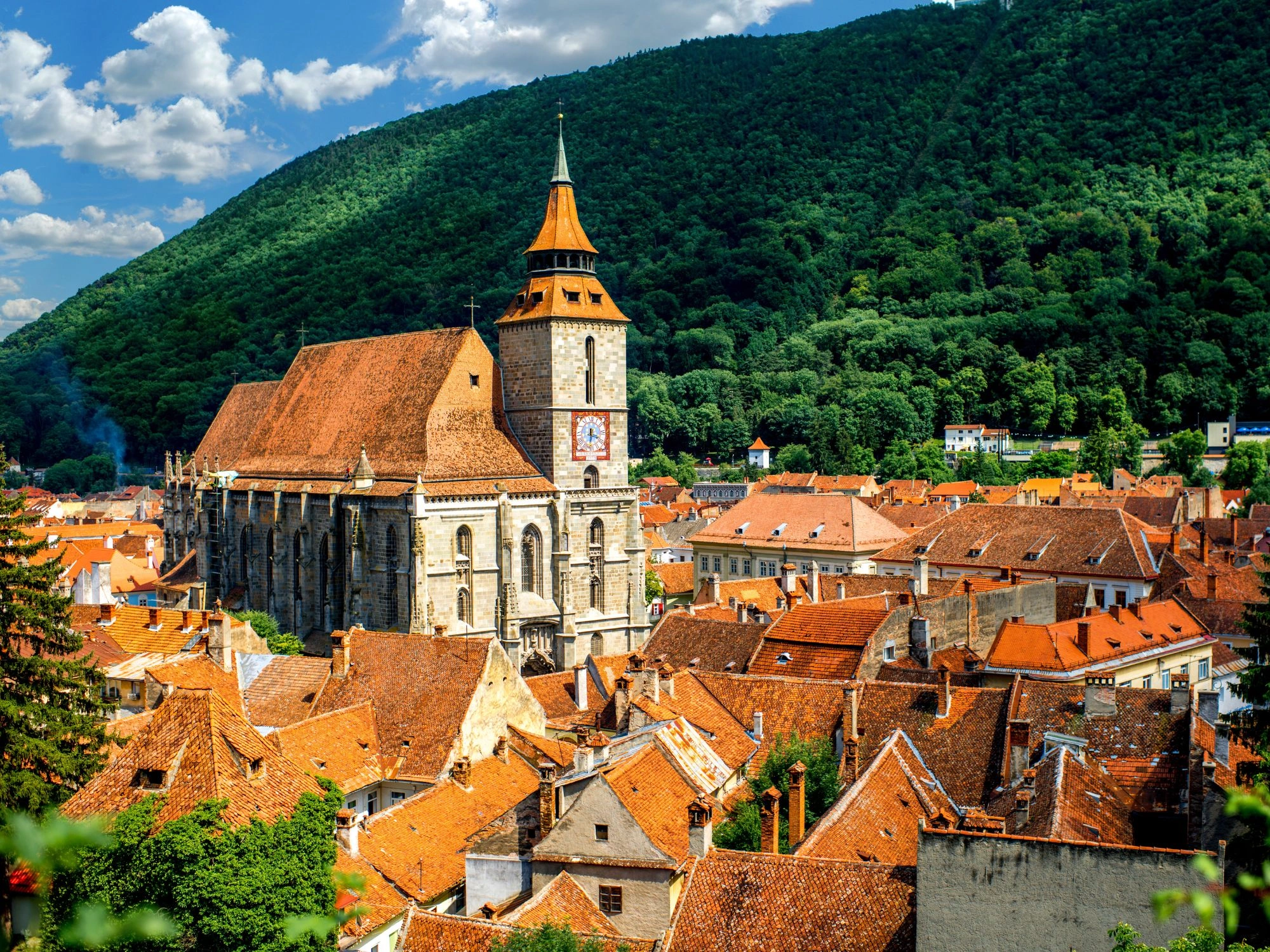 Brasov’s old town with red-tiled rooftops and the iconic Black Church under green hills.