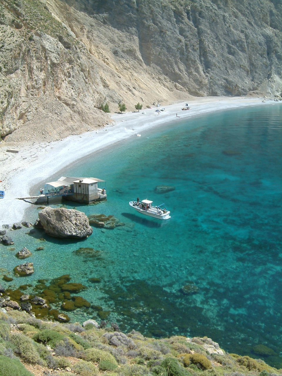 Clear turquoise sea at Sweetwater Beach with boat and rocky cliffs.