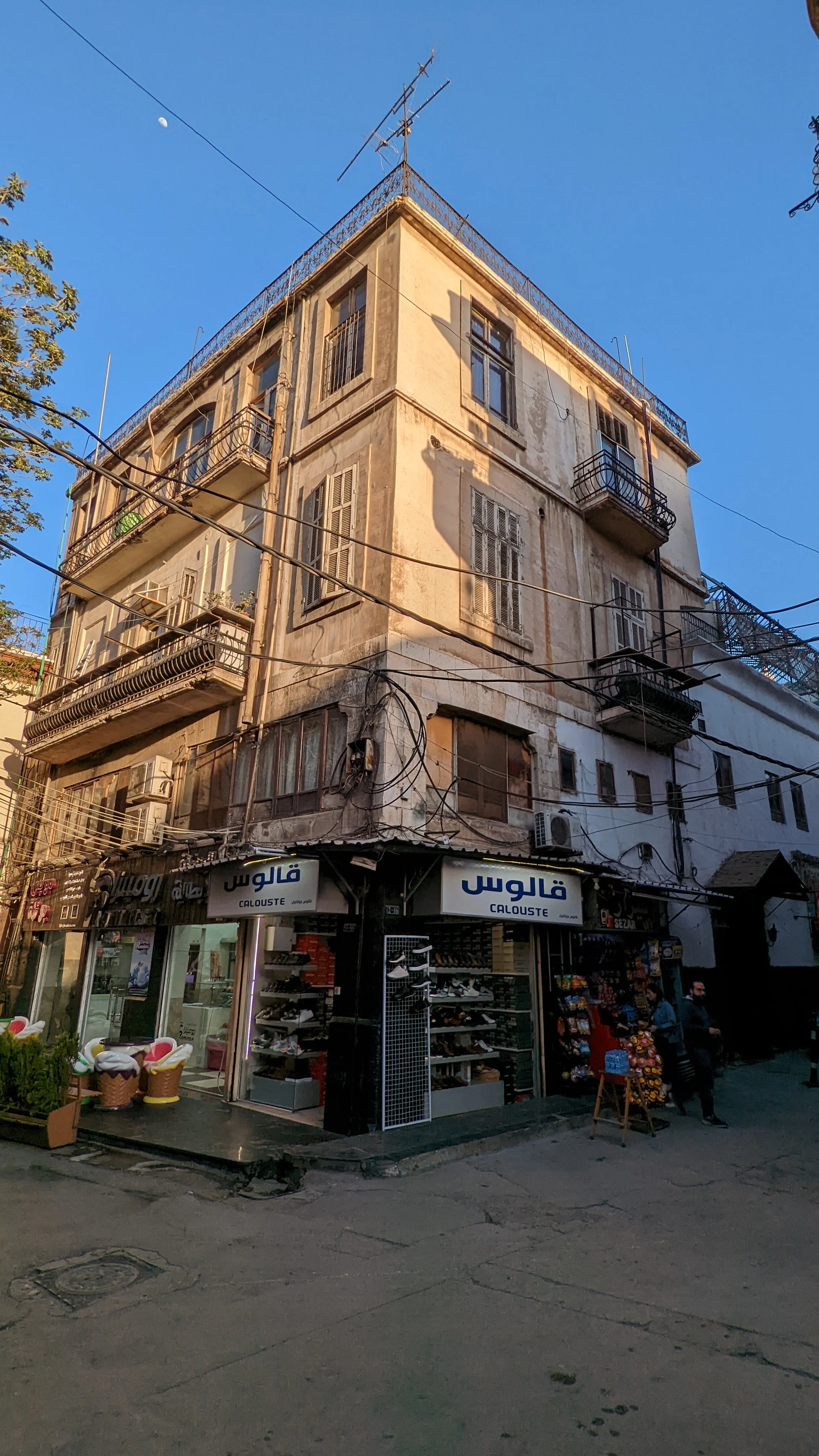 Old corner building in Damascus with balconies, exposed wiring, and street-level shops