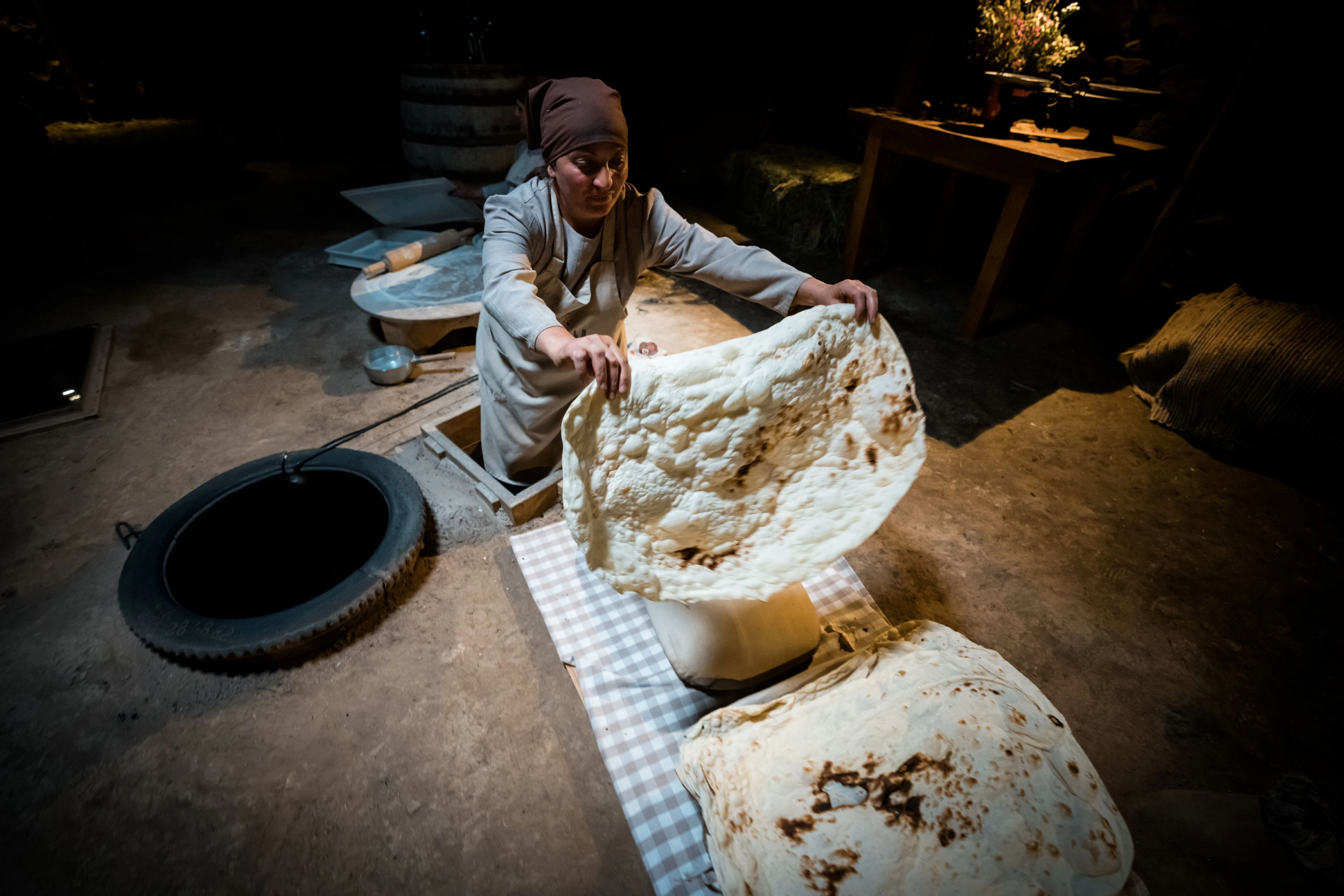 Armenian lavash making – woman baking traditional lavash bread over a tandoor oven in a rustic village bakery.