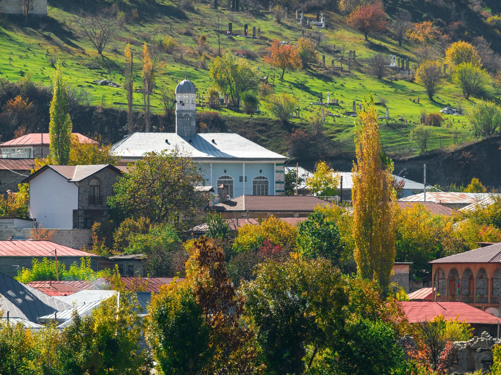 Caucasus village scene – autumn hillside village with colorful trees and a white domed church in the Caucasus mountains.