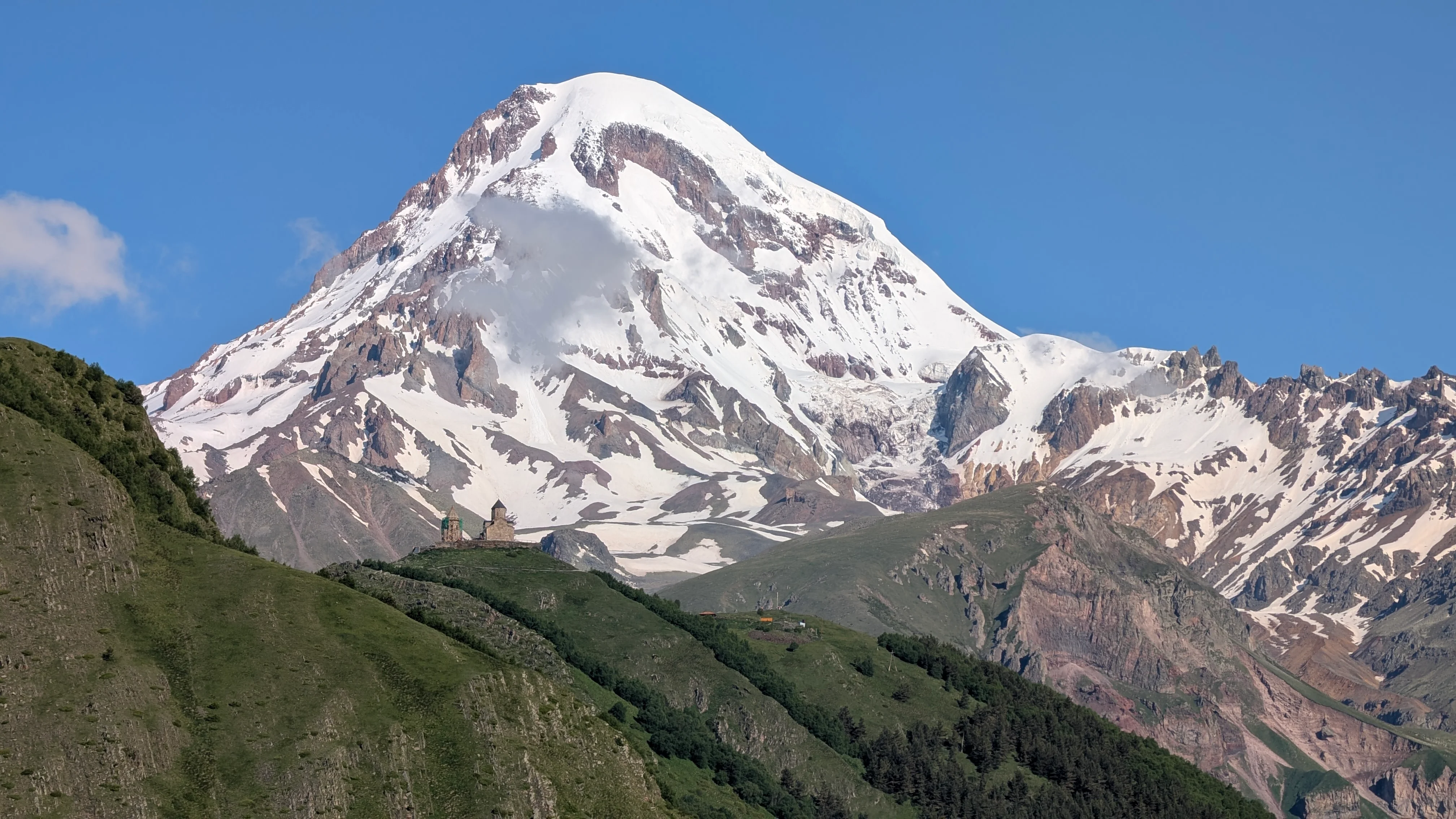 Mount Kazbek Georgia – snow‑capped Mount Kazbek towering over lush green hills and a tiny church in the Kazbegi region.