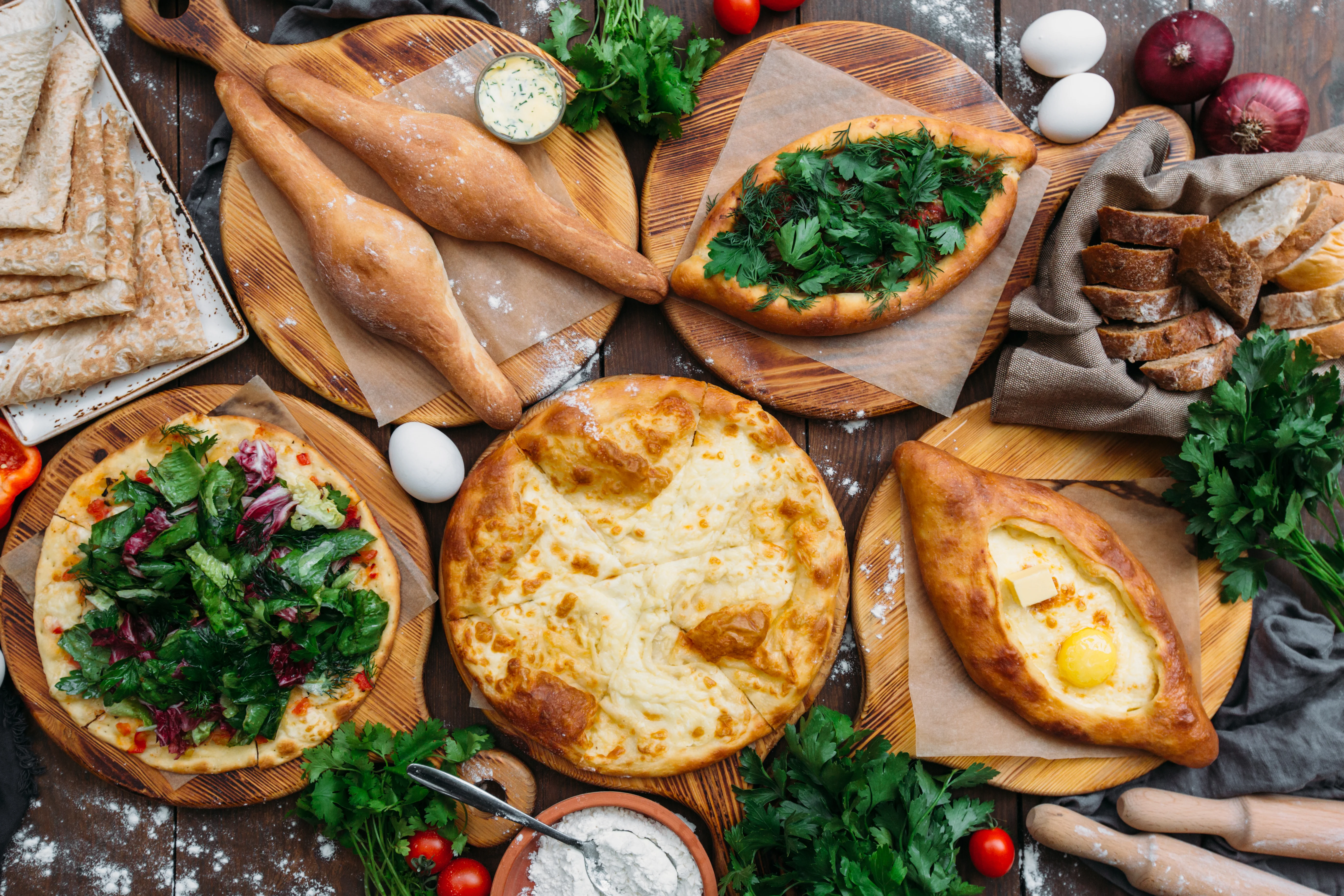 Georgian feast – overhead view of a traditional Georgian meal with khachapuri bread, salads, herbs and eggs.