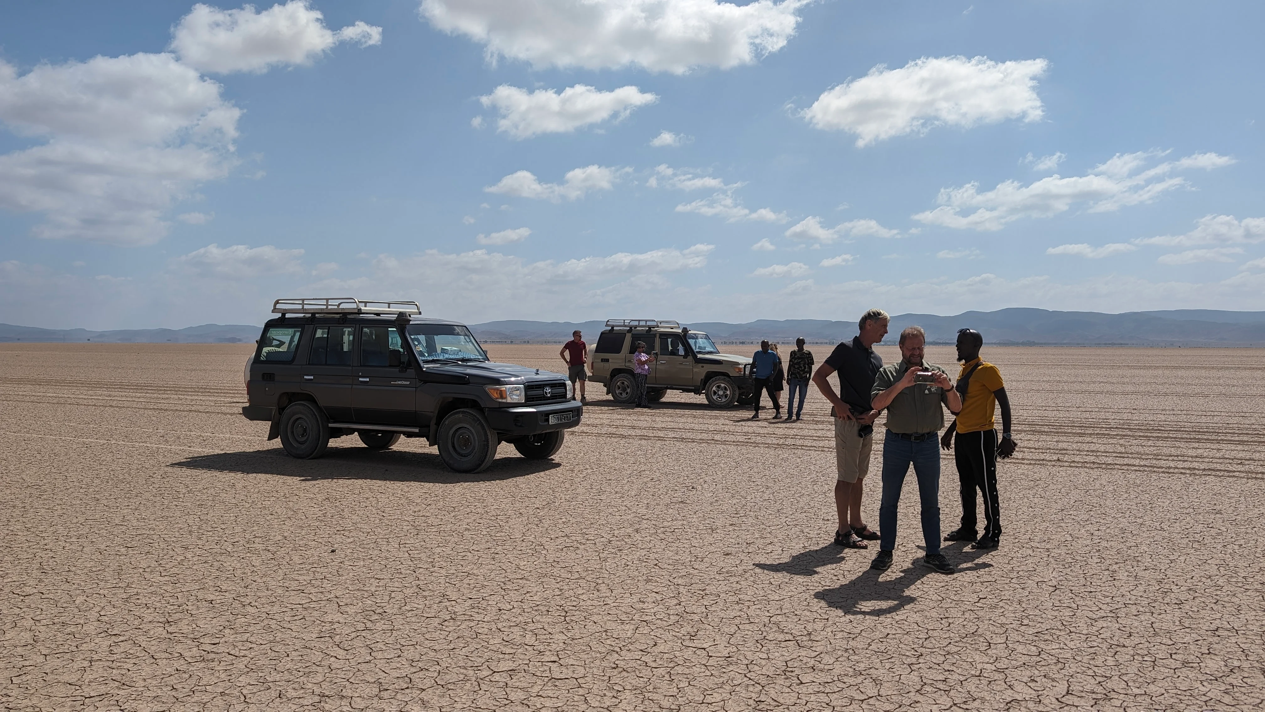 Tourists standing near 4x4 vehicles on dry cracked desert plain in Djibouti travel tour.