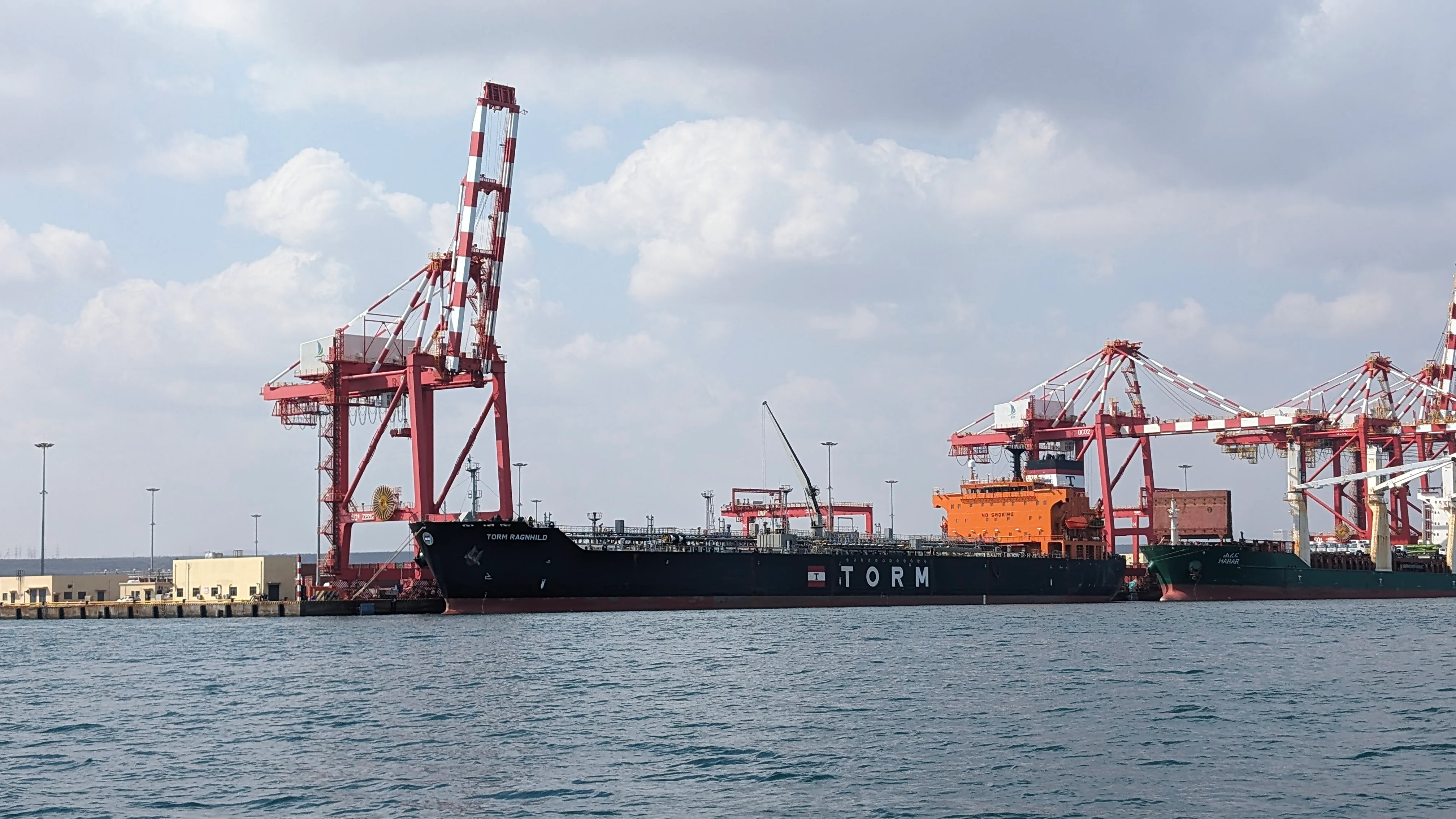Large cargo ship docked at Djibouti port with red cranes and cloudy sky.