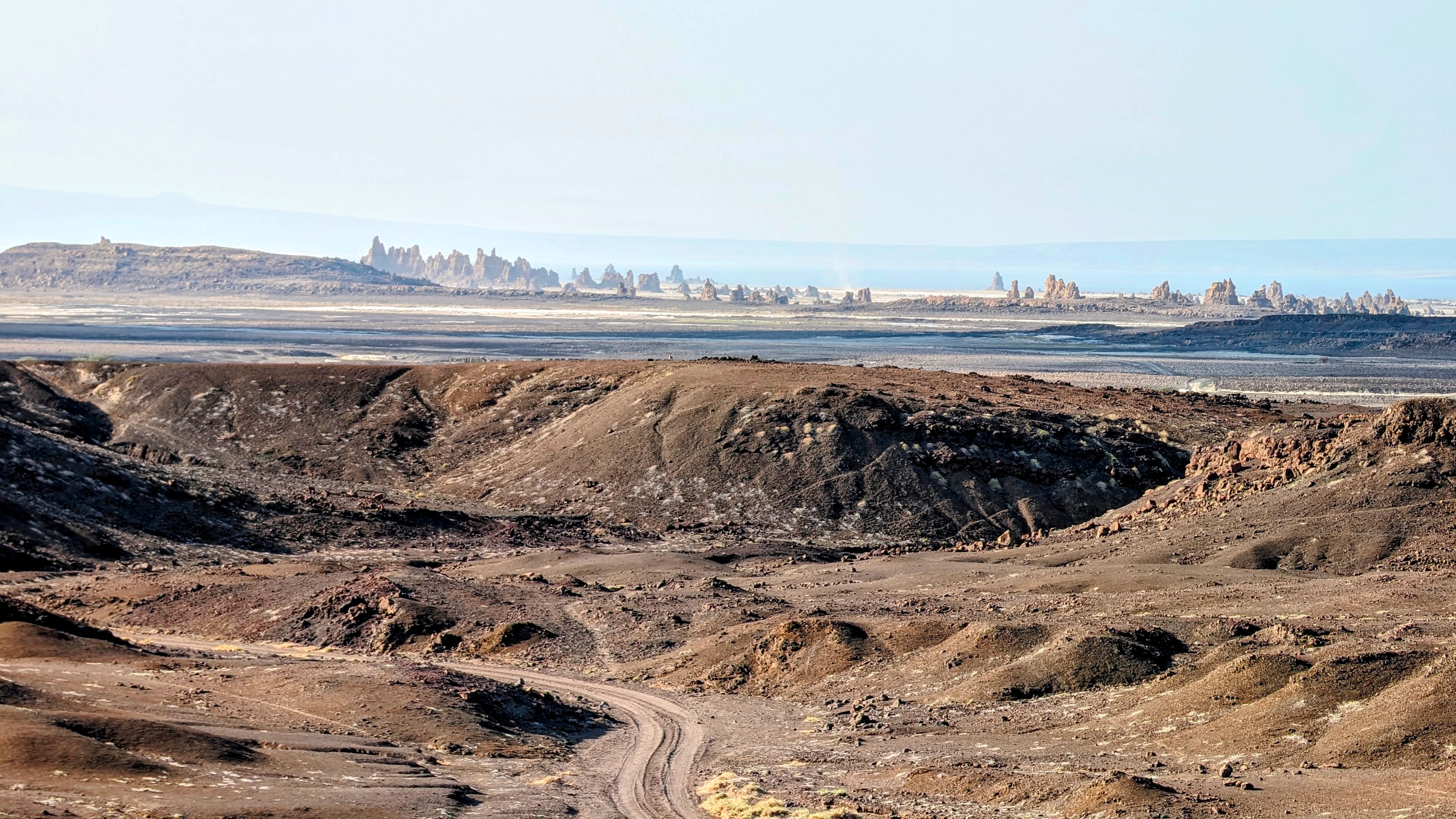 Rocky volcanic landscape with distant limestone chimneys in Djibouti’s Lake Abbe region.