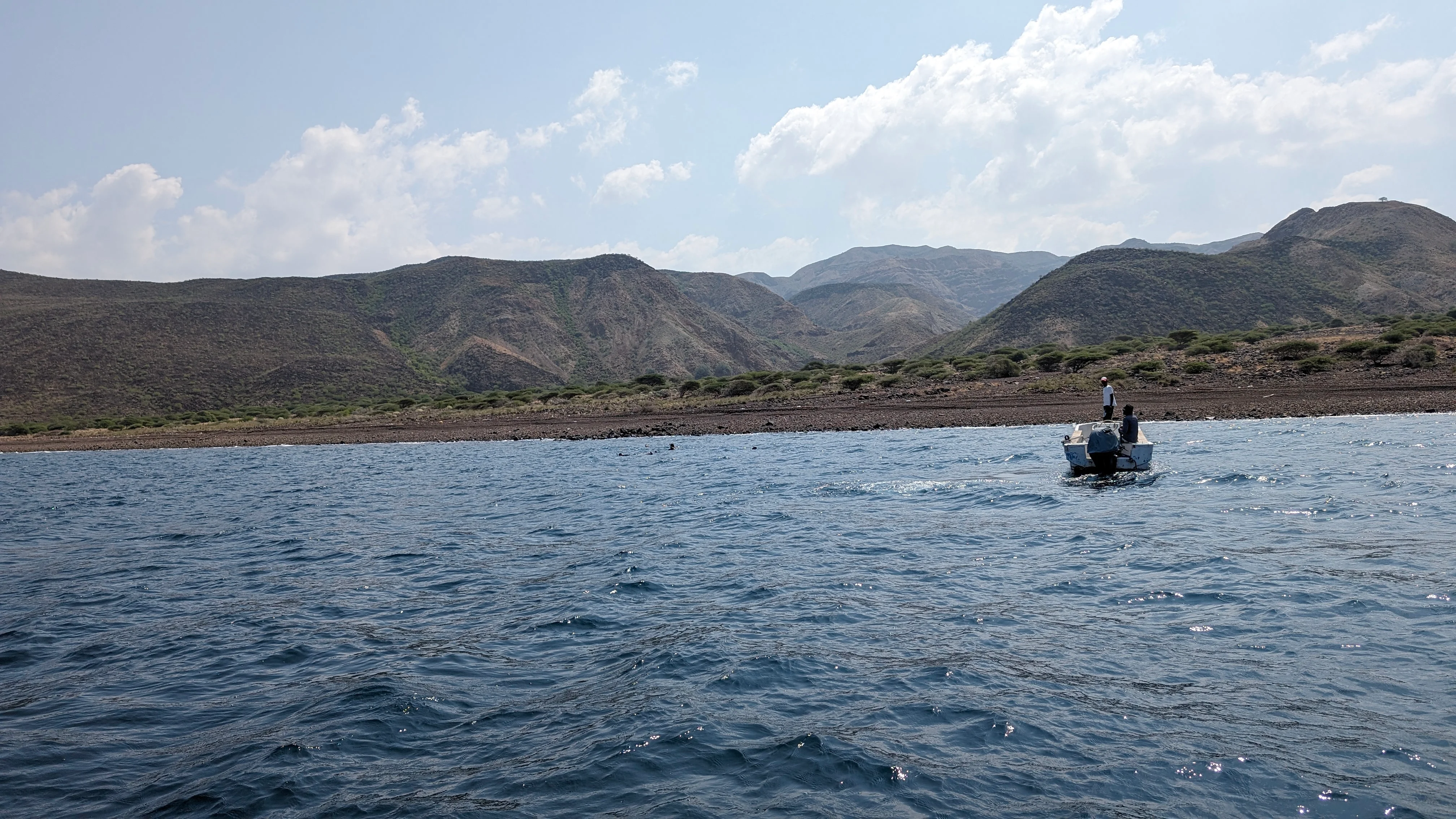 Small boat with people near rocky coastline and green hills in Djibouti.