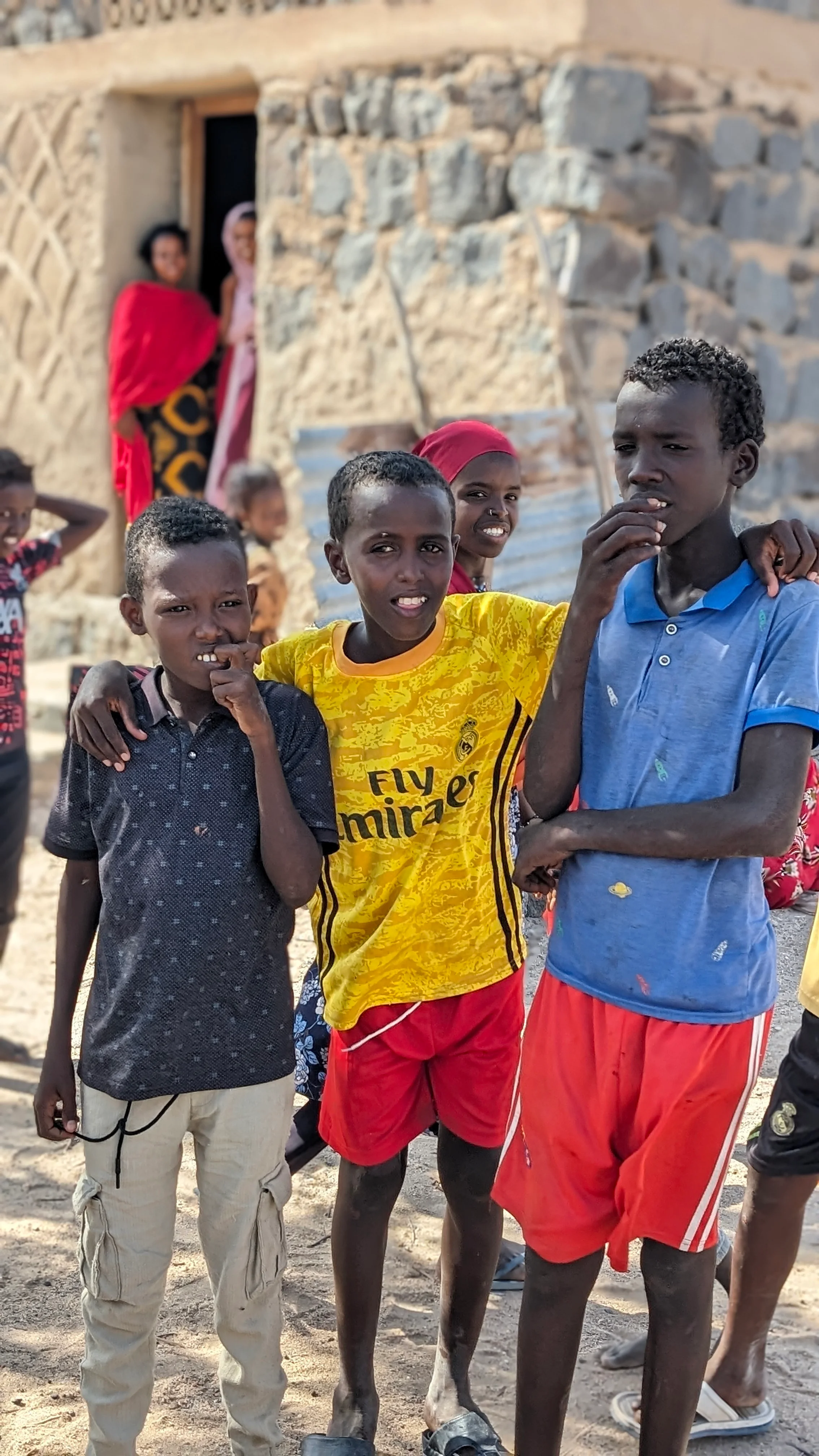 Smiling boys pose outside stone house in rural Djibouti village during cultural visit.