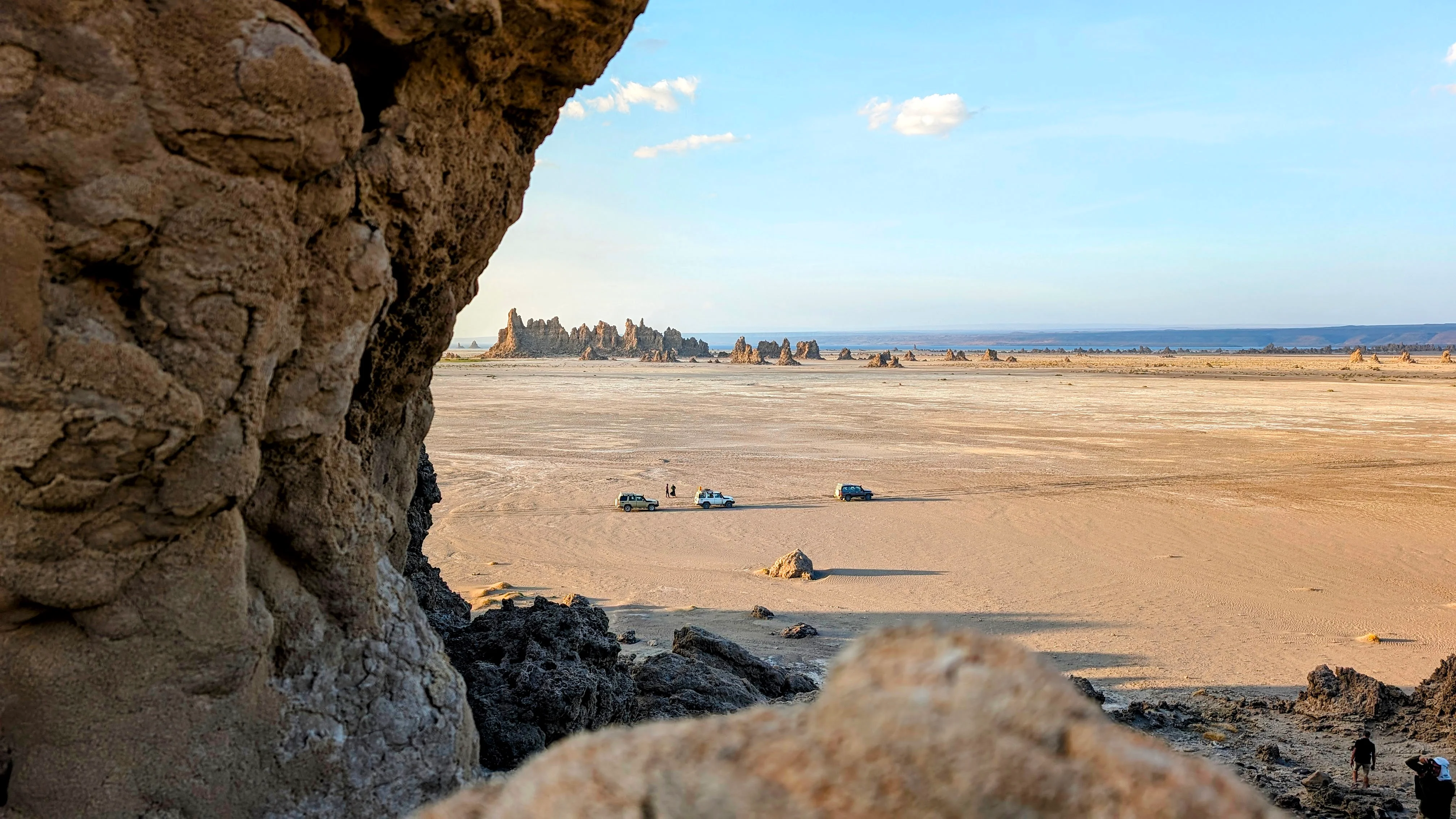 Framed view of desert and 4x4s through rock at Lake Abbe in Djibouti.