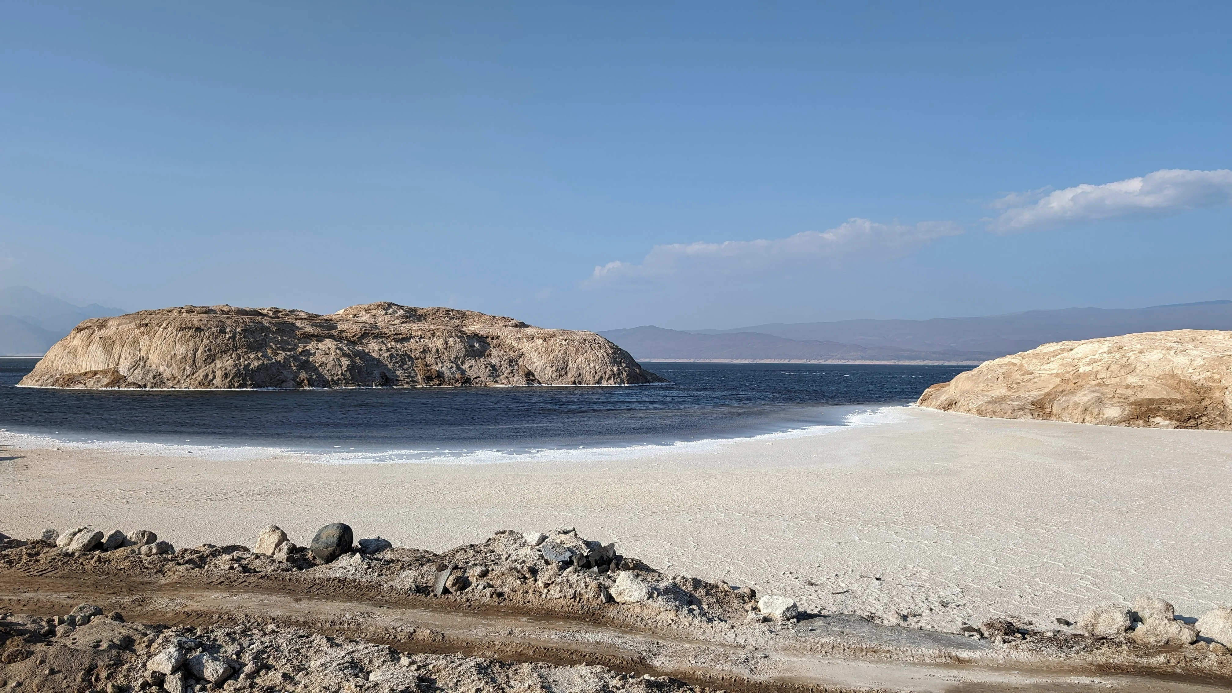 Salt-lined shores and rocky islands of Lake Assal under blue sky in Djibouti.