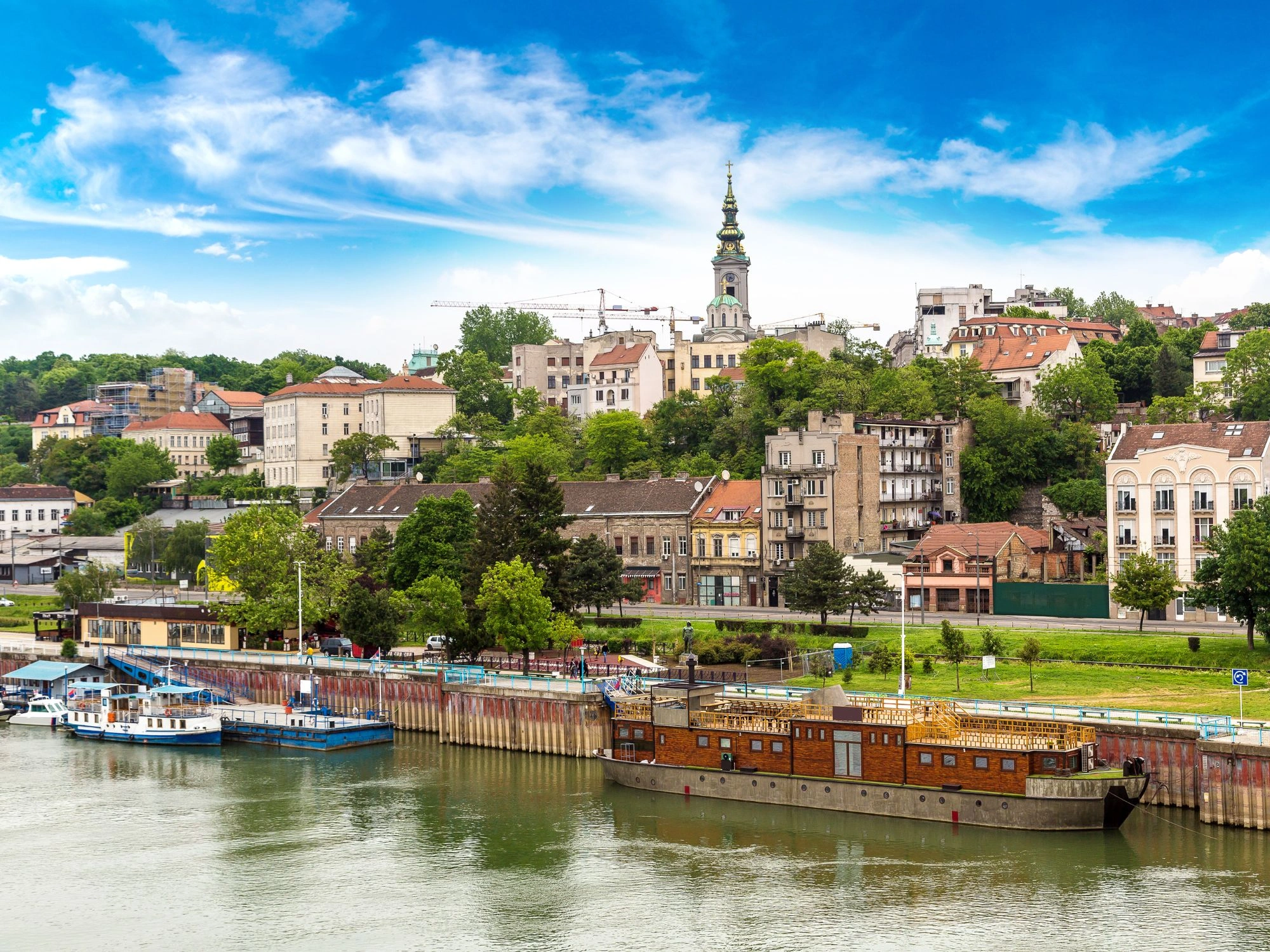 Historic Belgrade waterfront with church spire, riverside buildings and boats along the Sava River in Serbia.