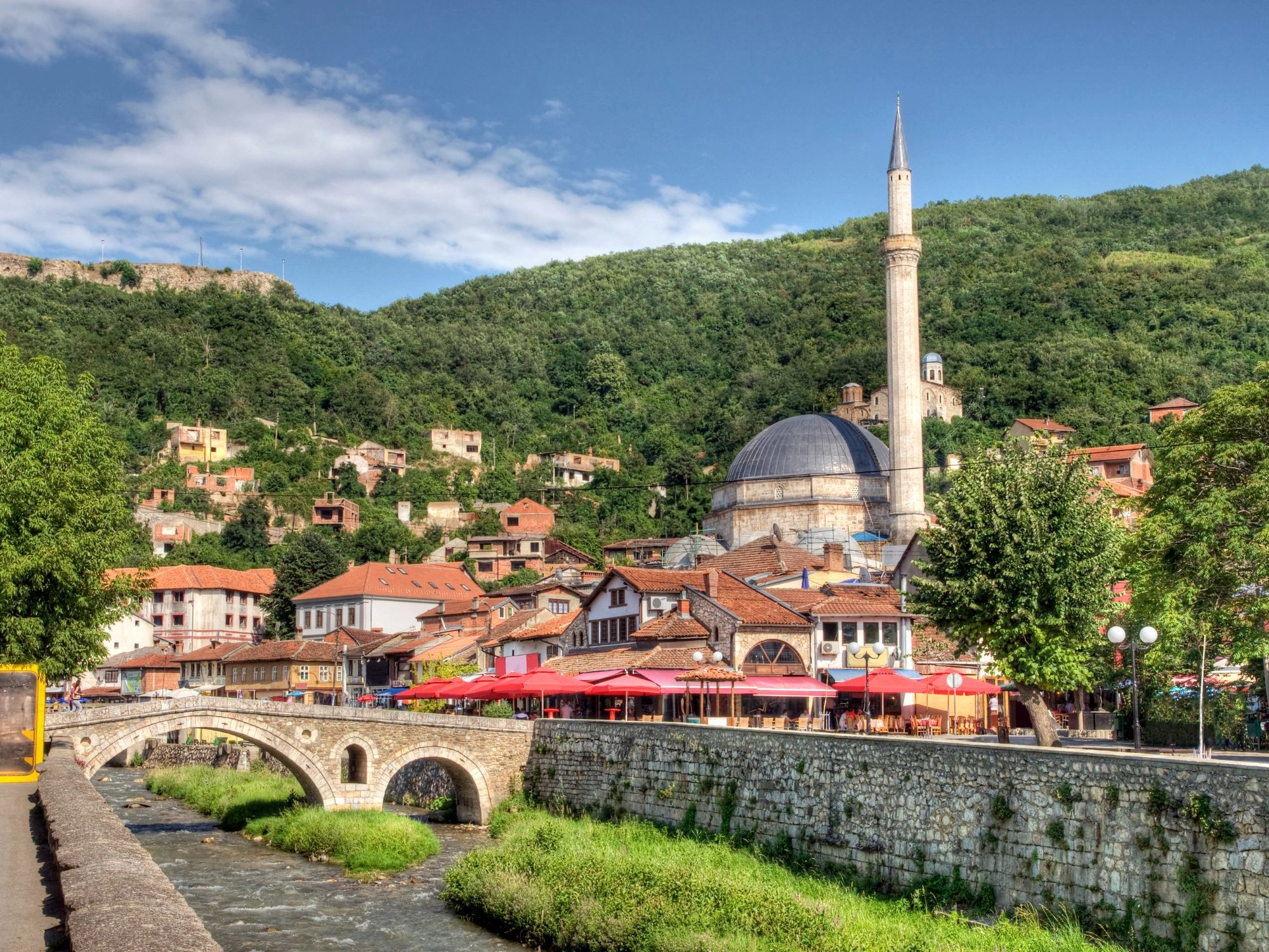 Sinan Pasha Mosque and stone bridge over a river with hillside village in Prizren, Kosovo.