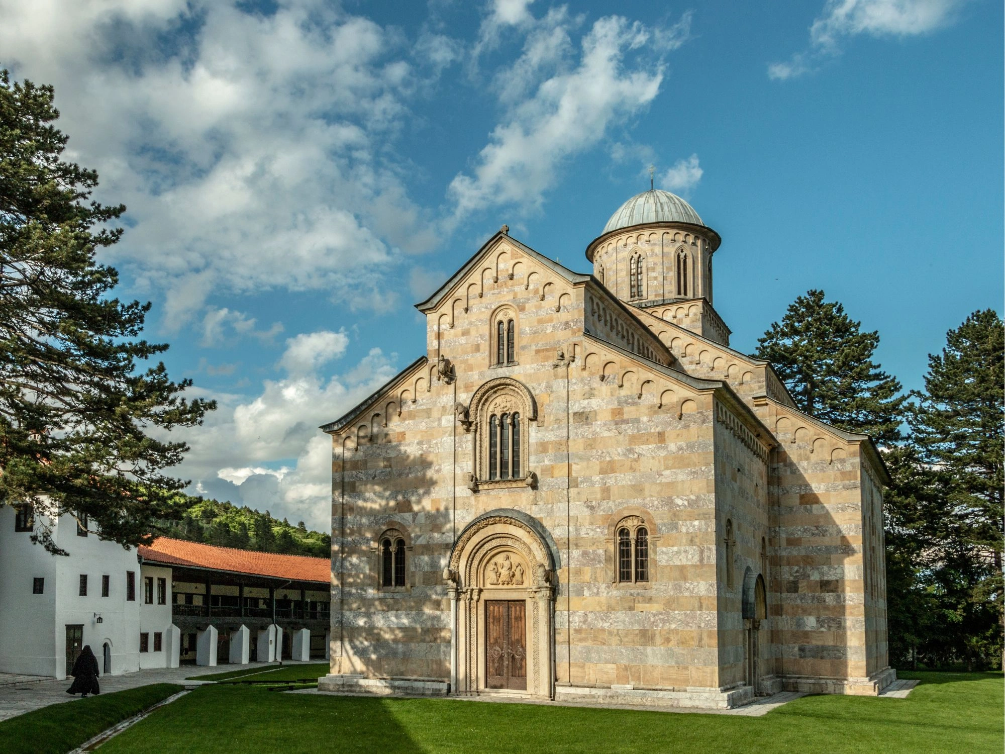 Striped stone Visoki Dečani Monastery with domed roof surrounded by pine trees in Kosovo.