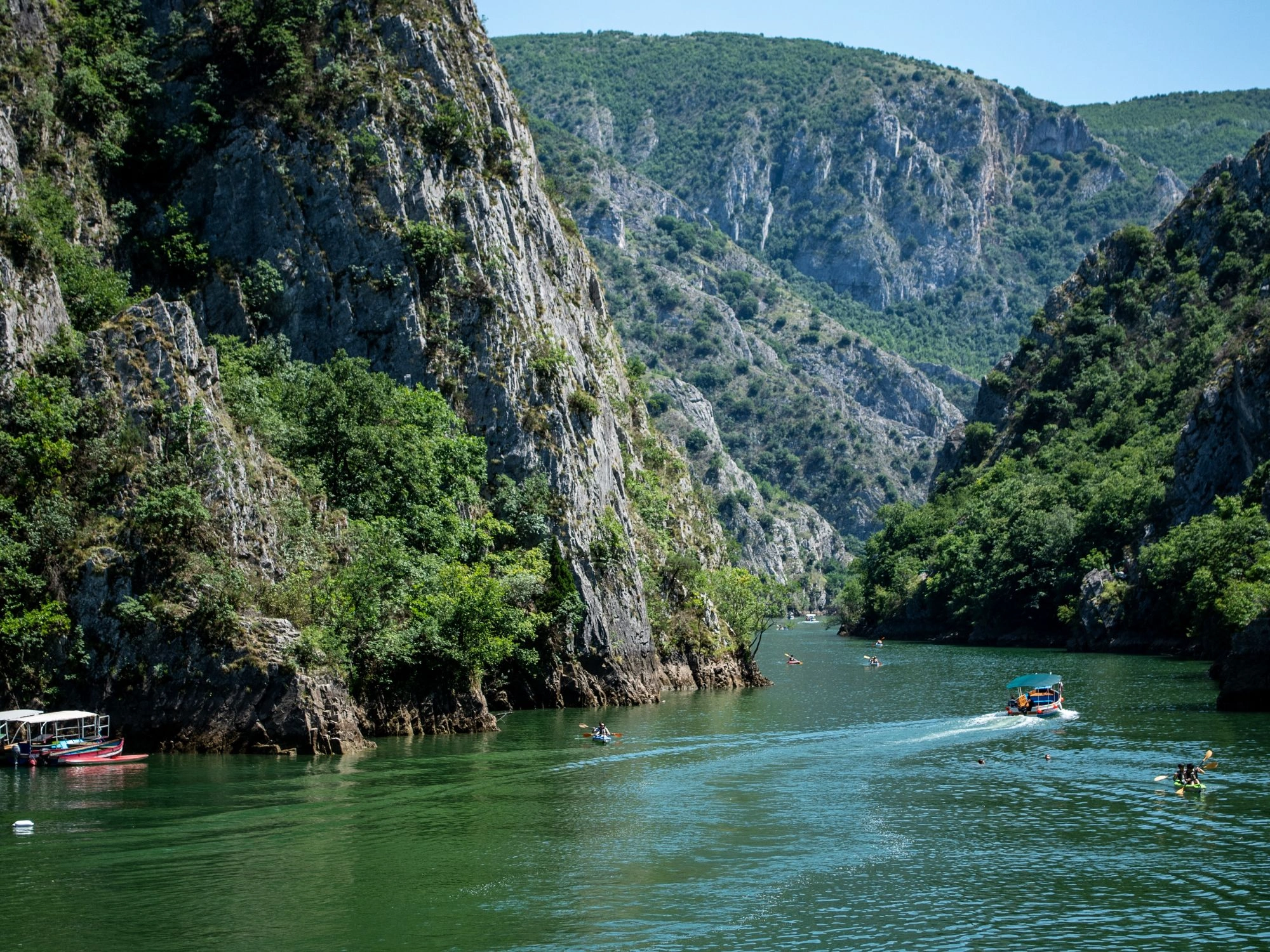 Kayakers and boat on emerald Matka Canyon river winding between steep cliffs in North Macedonia.