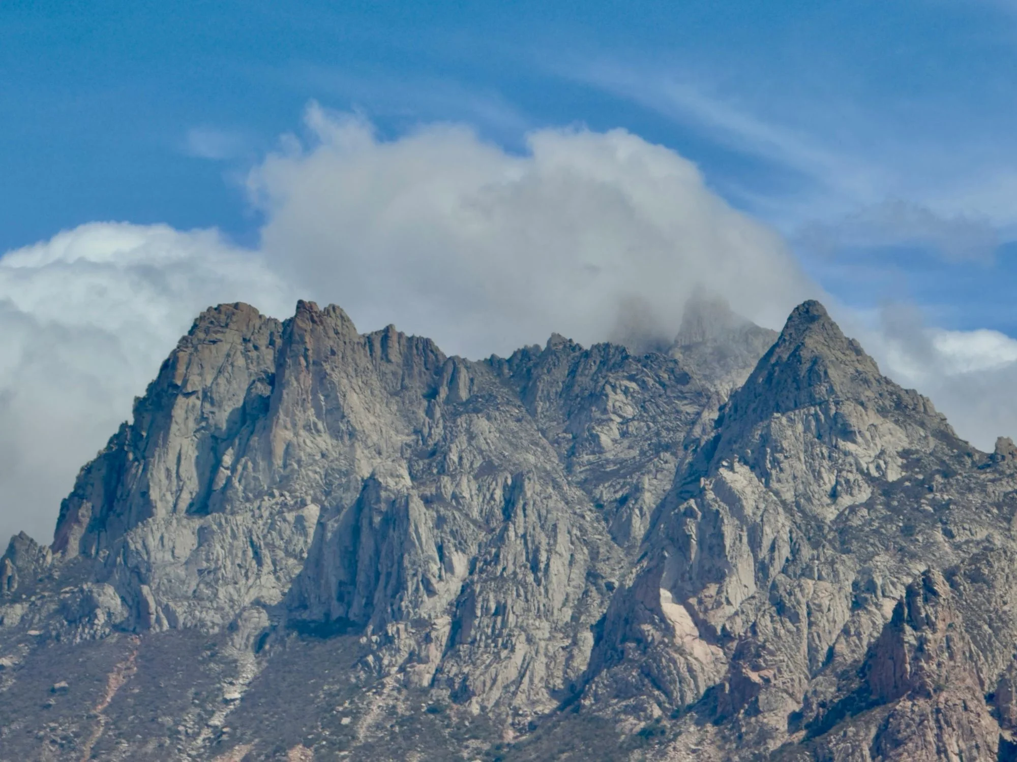 Rugged peaks of Socotra’s Haghier Mountains emerging from clouds under blue sky.
