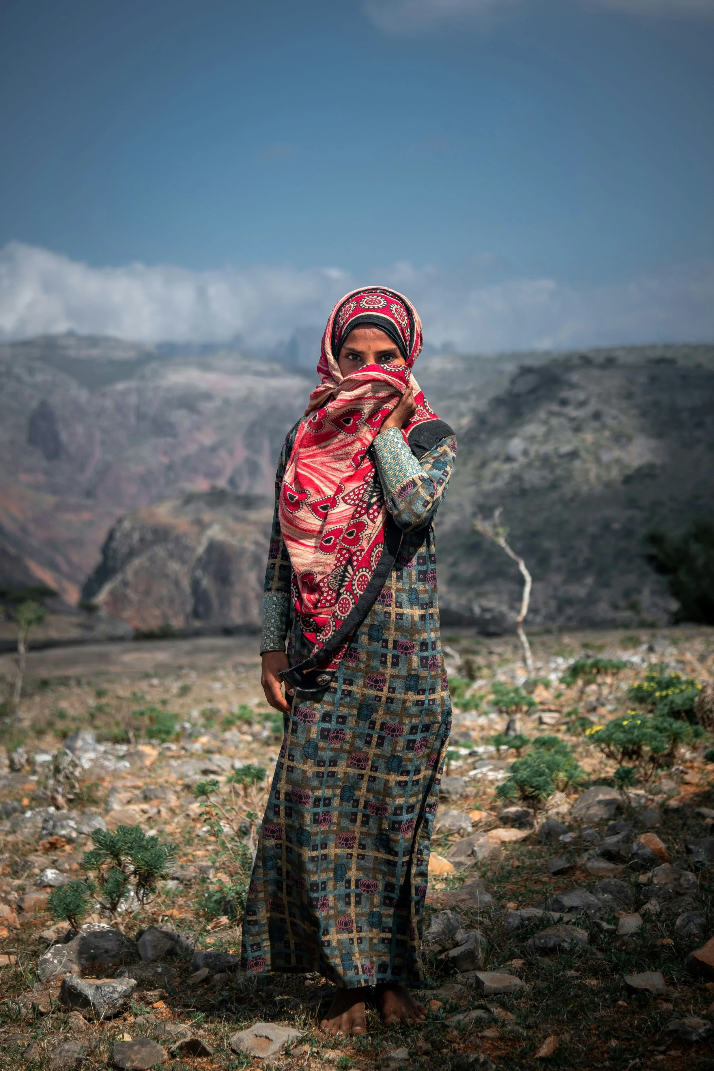 Young girl in colorful dress standing in Socotra’s rugged mountain landscape with dramatic rocky backdrop.