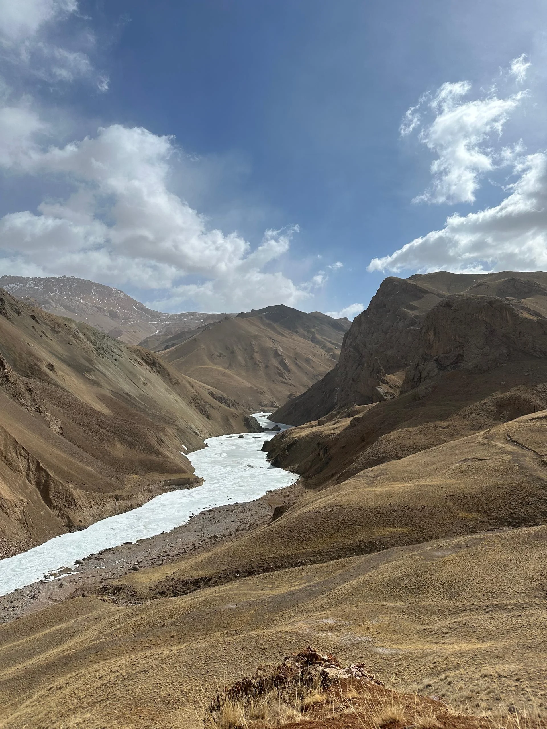 Frozen milky-white river winding through a wide high-altitude valley flanked by brown mountain slopes, Tien Shan, Kyrgyzstan