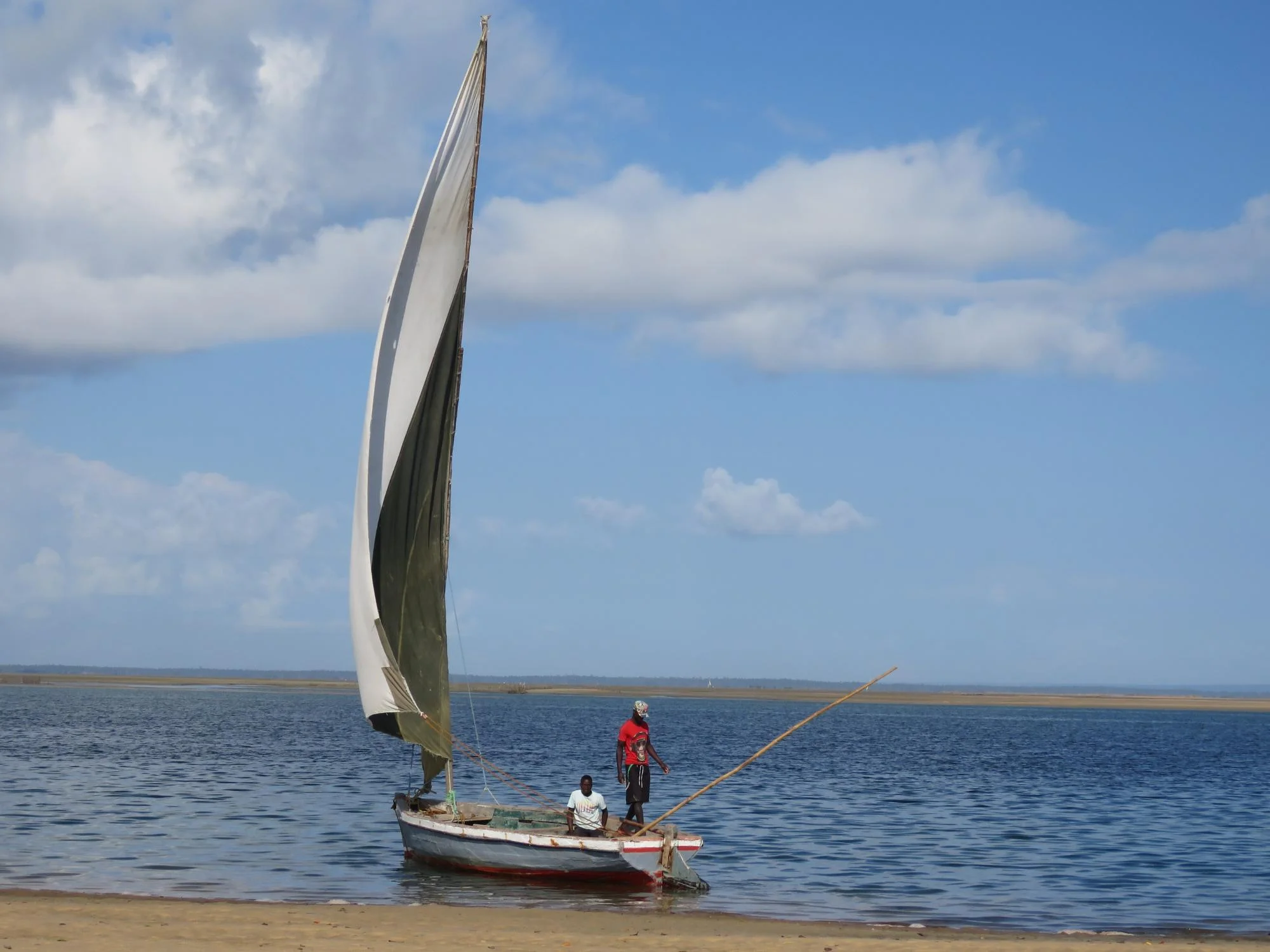 Two fishermen aboard a traditional wooden sailing dhow beached on a sandy Mozambican shoreline
