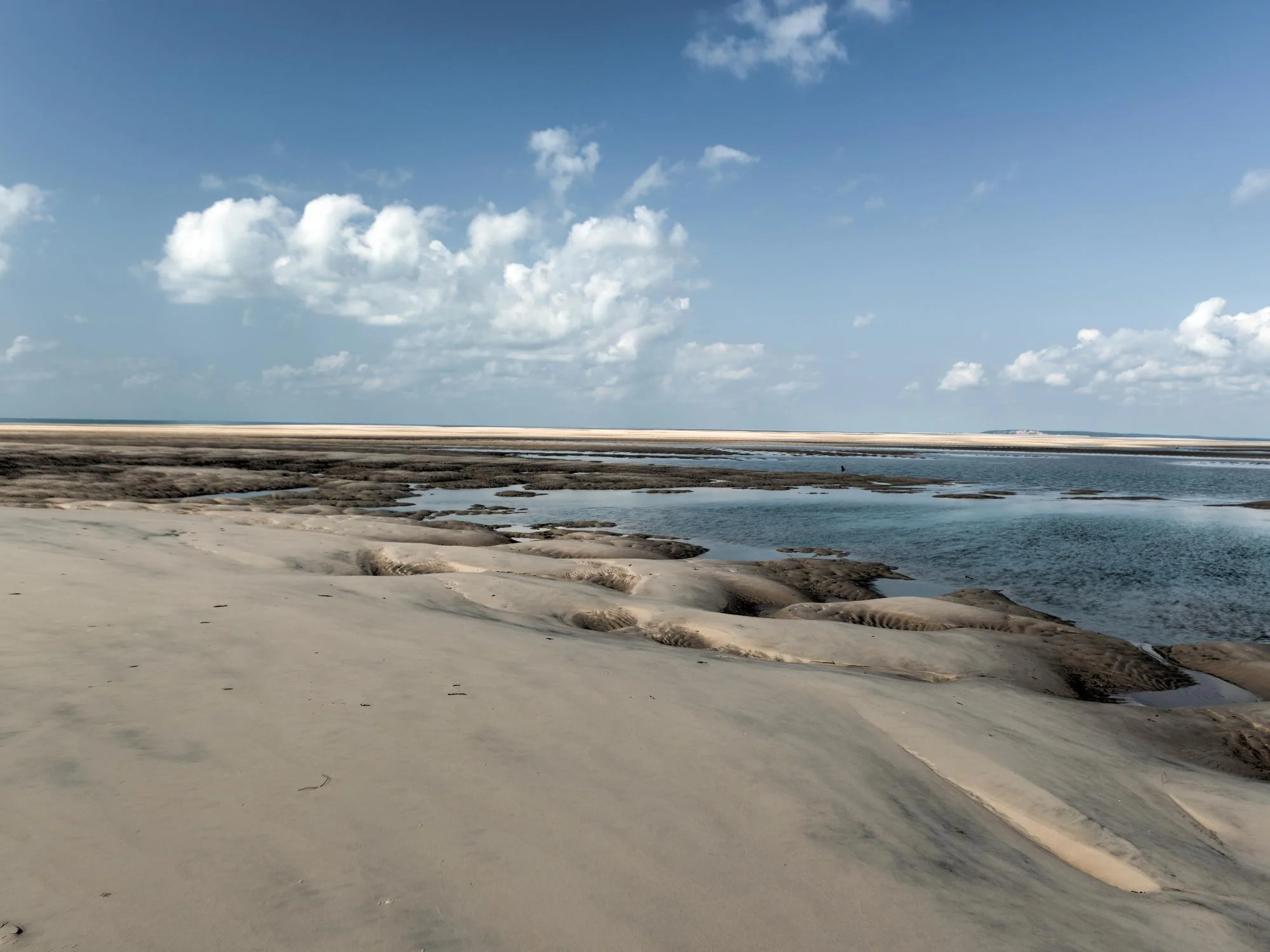 Wide shallow tidal estuary with exposed sandy flats and rock pools under a partly cloudy sky, Mozambique