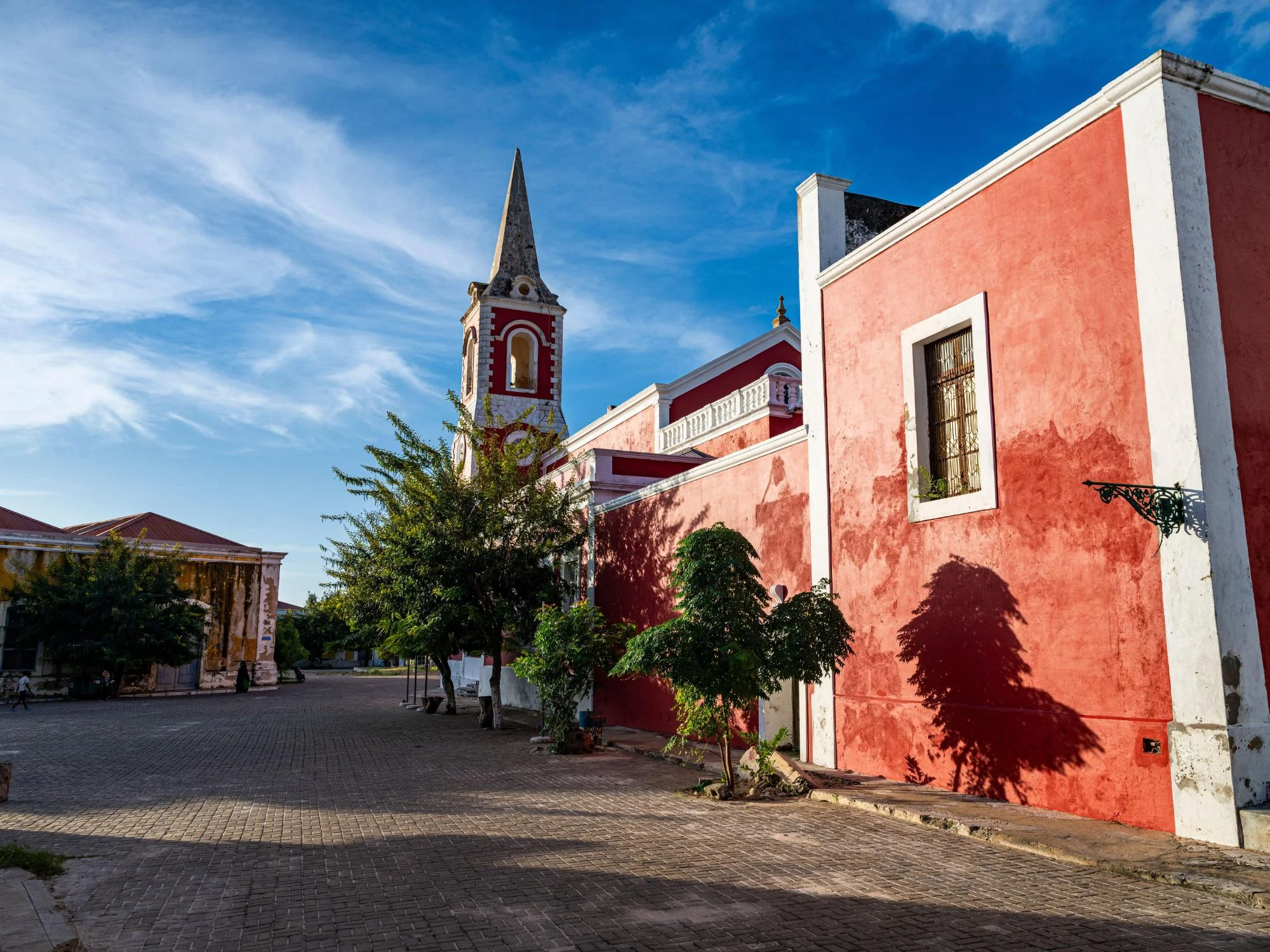 Cobblestone square in Inhambane lined with red colonial buildings and a church bell tower, Mozambique