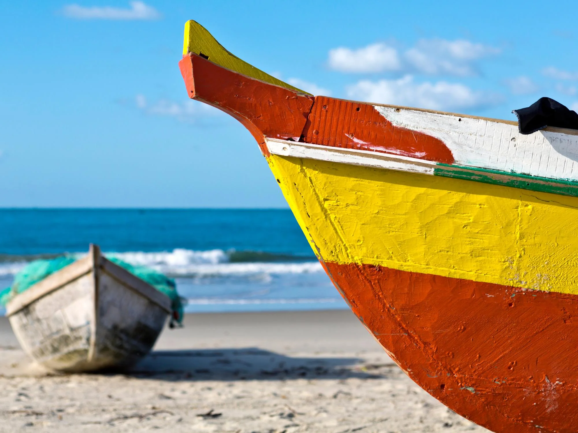 Close-up of the bow of a brightly painted red and yellow wooden fishing dhow beached on the Mozambique coast