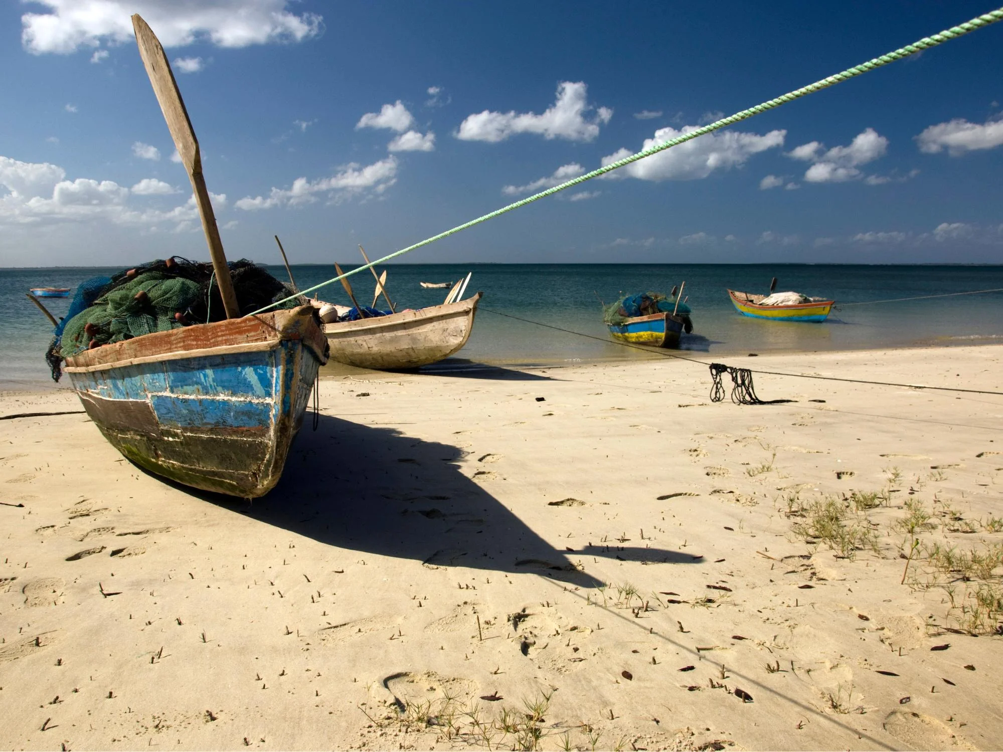 Wooden fishing dhows loaded with nets resting on a sandy beach under a blue sky on the Mozambique coast