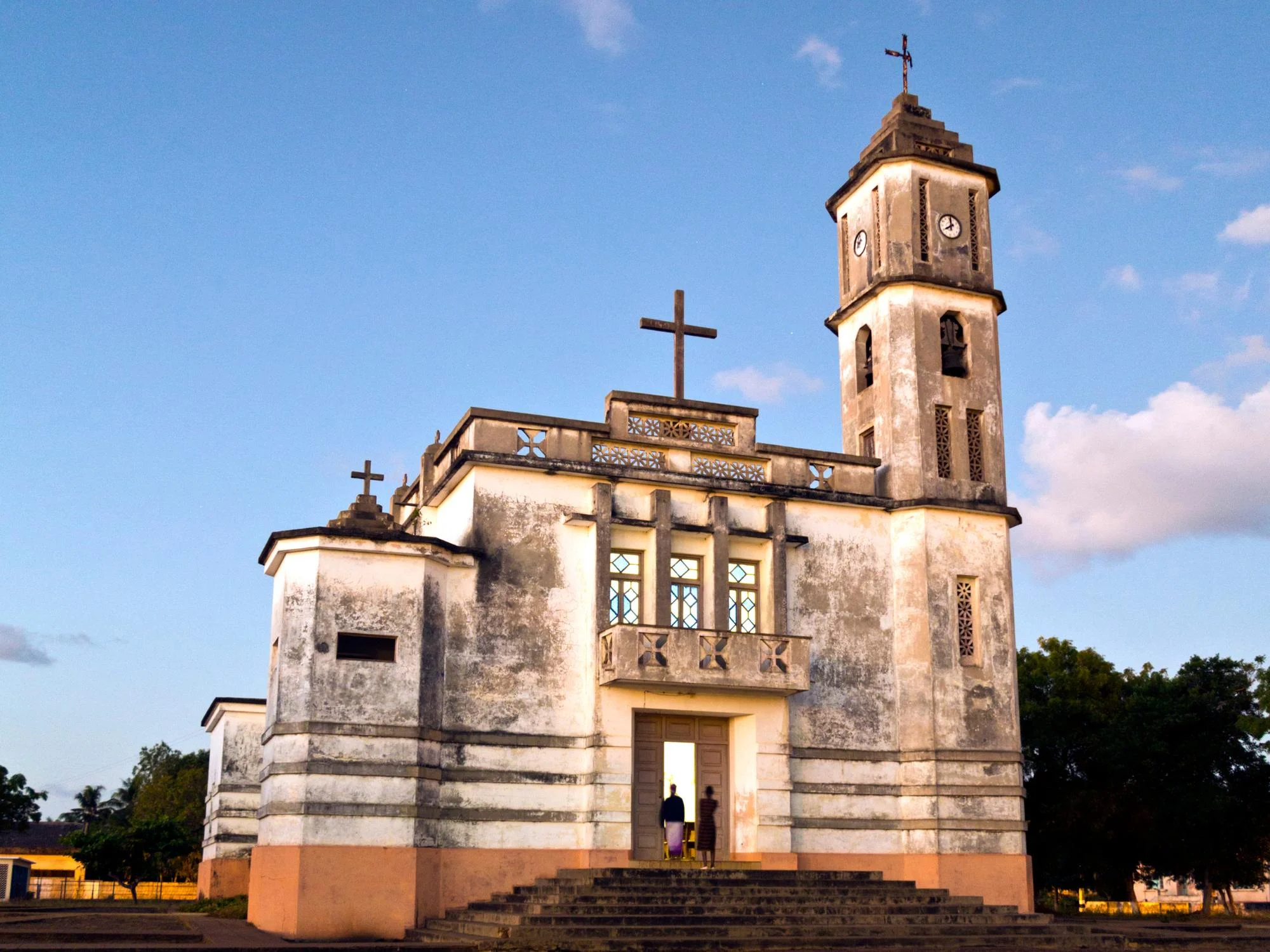Colonial-era church bathed in golden evening light with two figures at its illuminated doorway, Mozambique