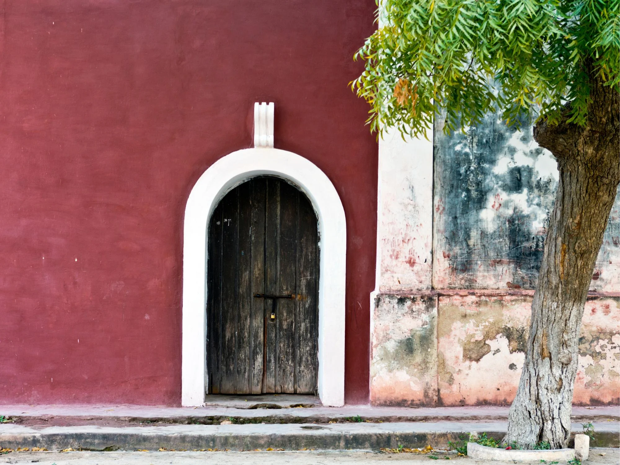 Aged wooden arched doorway set in a deep crimson colonial facade beside a weathered wall, Inhambane, Mozambique