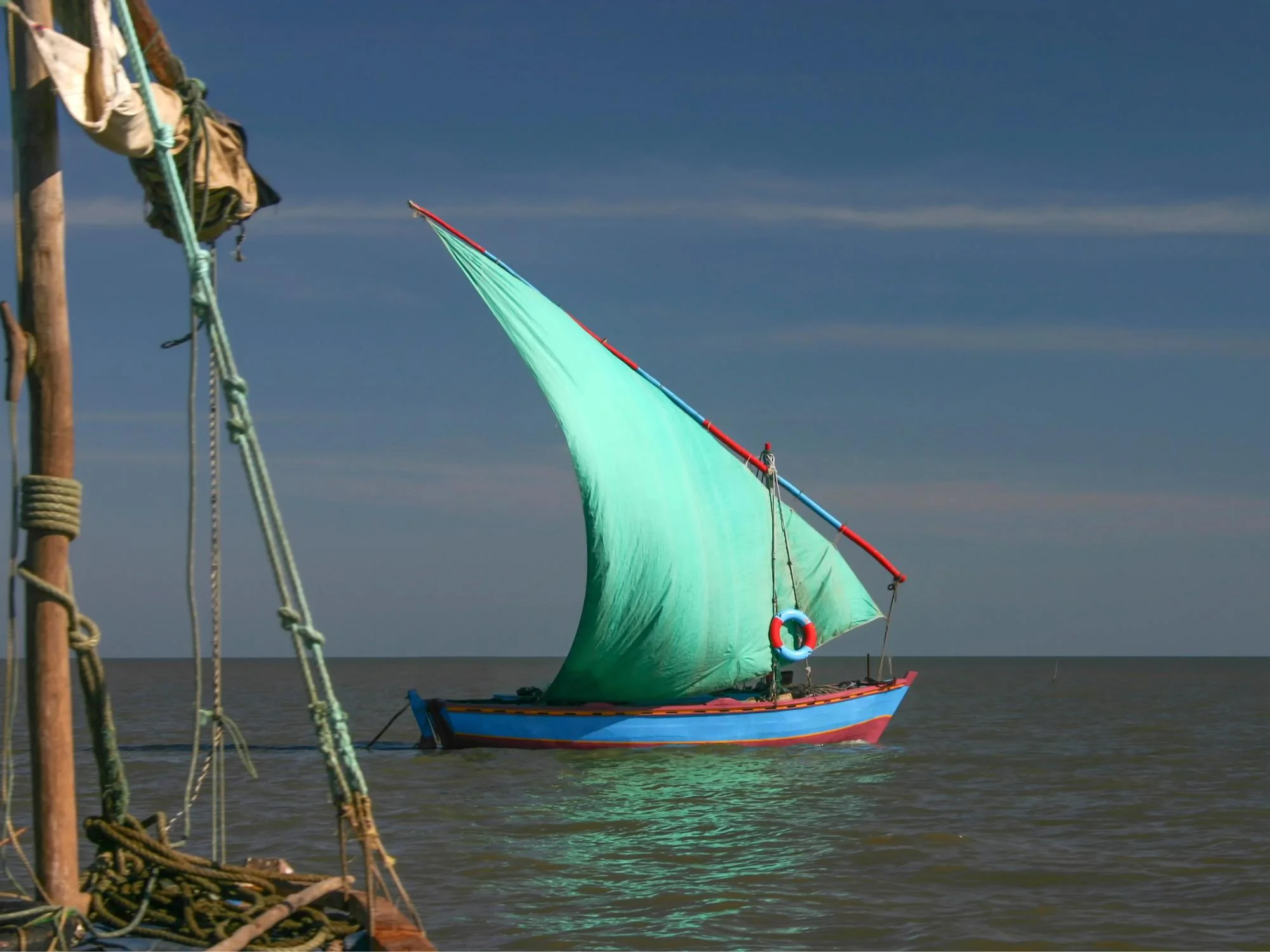 Blue dhow with a billowing turquoise triangular sail crossing calm open water off the Mozambique coast