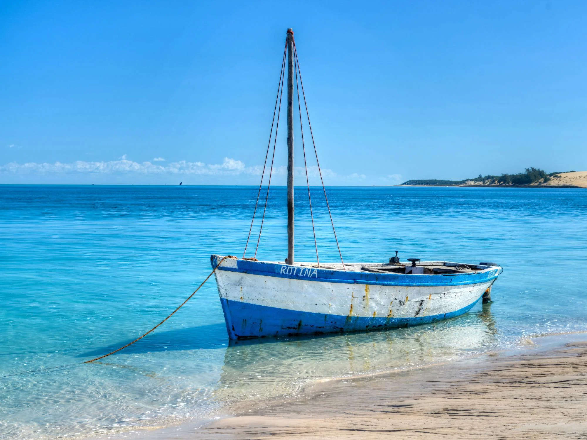 Blue and white wooden fishing dhow named Rotina moored in crystal-clear turquoise water on Mozambique's coast
