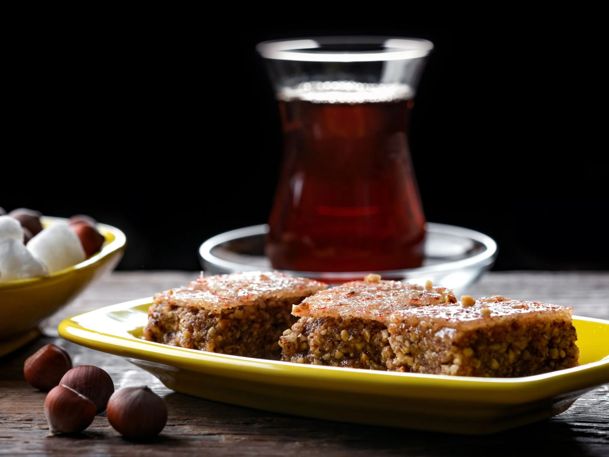 Pear-shaped armudu tea glass with golden Azerbaijani pakhlava and hazelnuts in a warm, moody still life