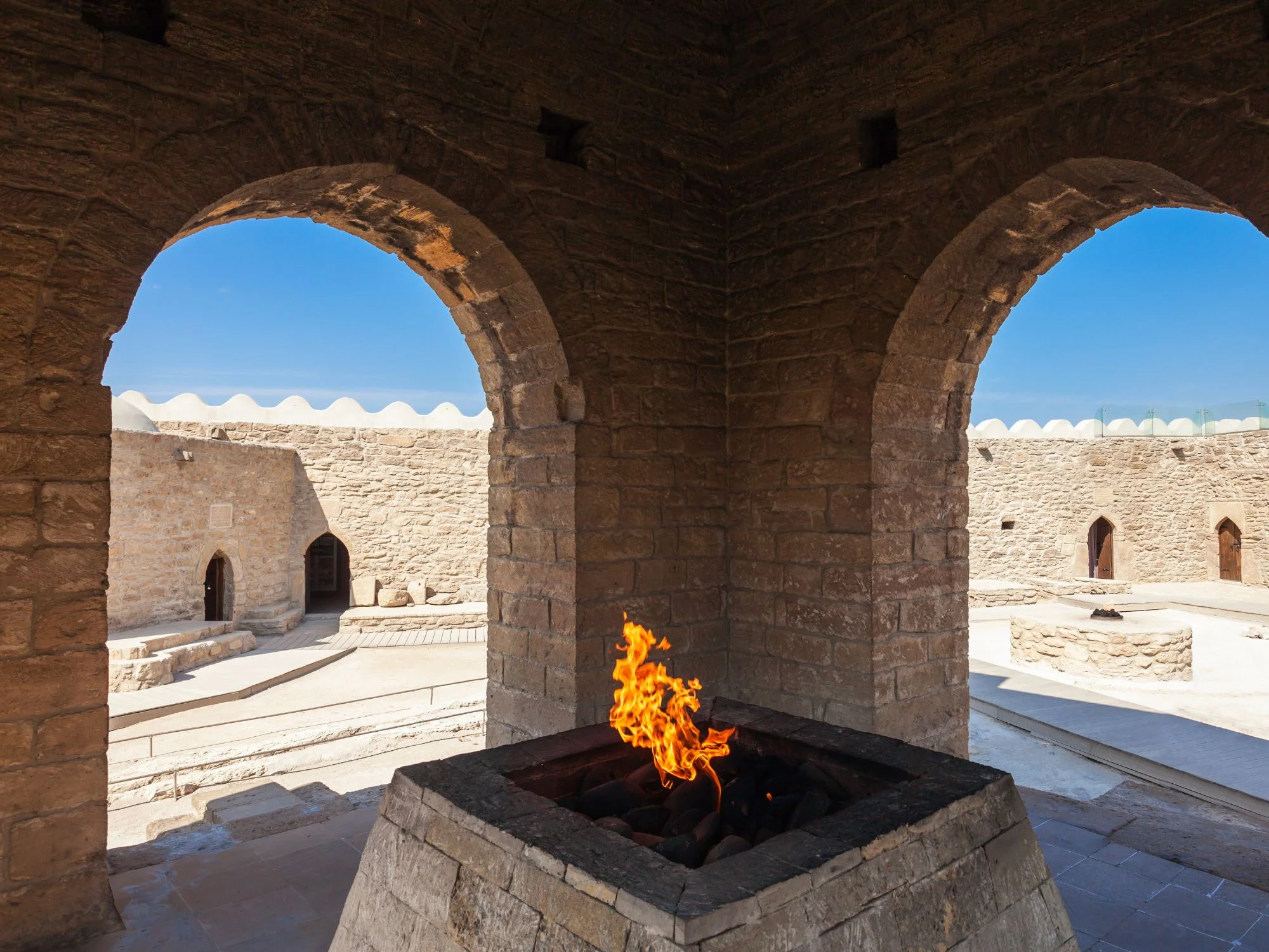 Eternal flame burning at the central altar of the Ateshgah Fire Temple, framed by stone arches of the courtyard