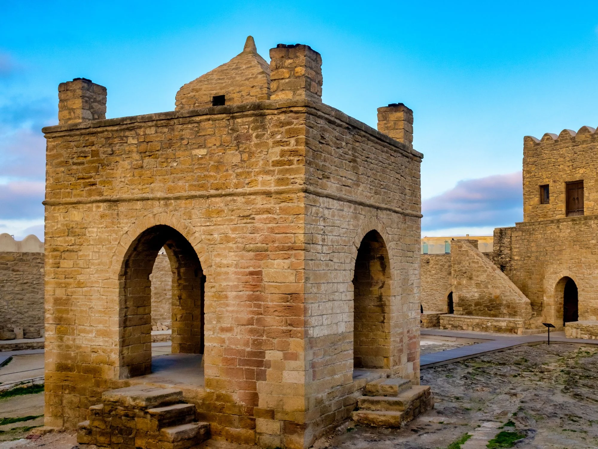 Outer stone walls and arches of the Ateshgah Fire Temple complex near Baku, under a clear blue sky
