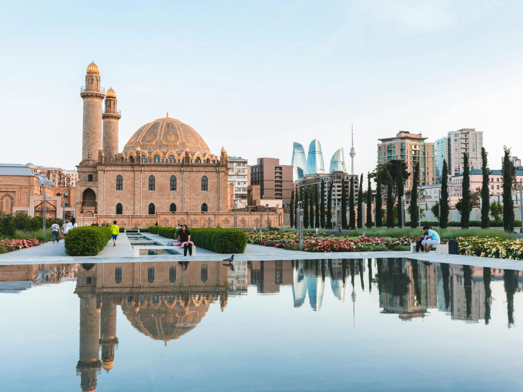 Grand twin-minaret mosque with central dome reflected in a pool, with the Baku skyline and Flame Towers behind