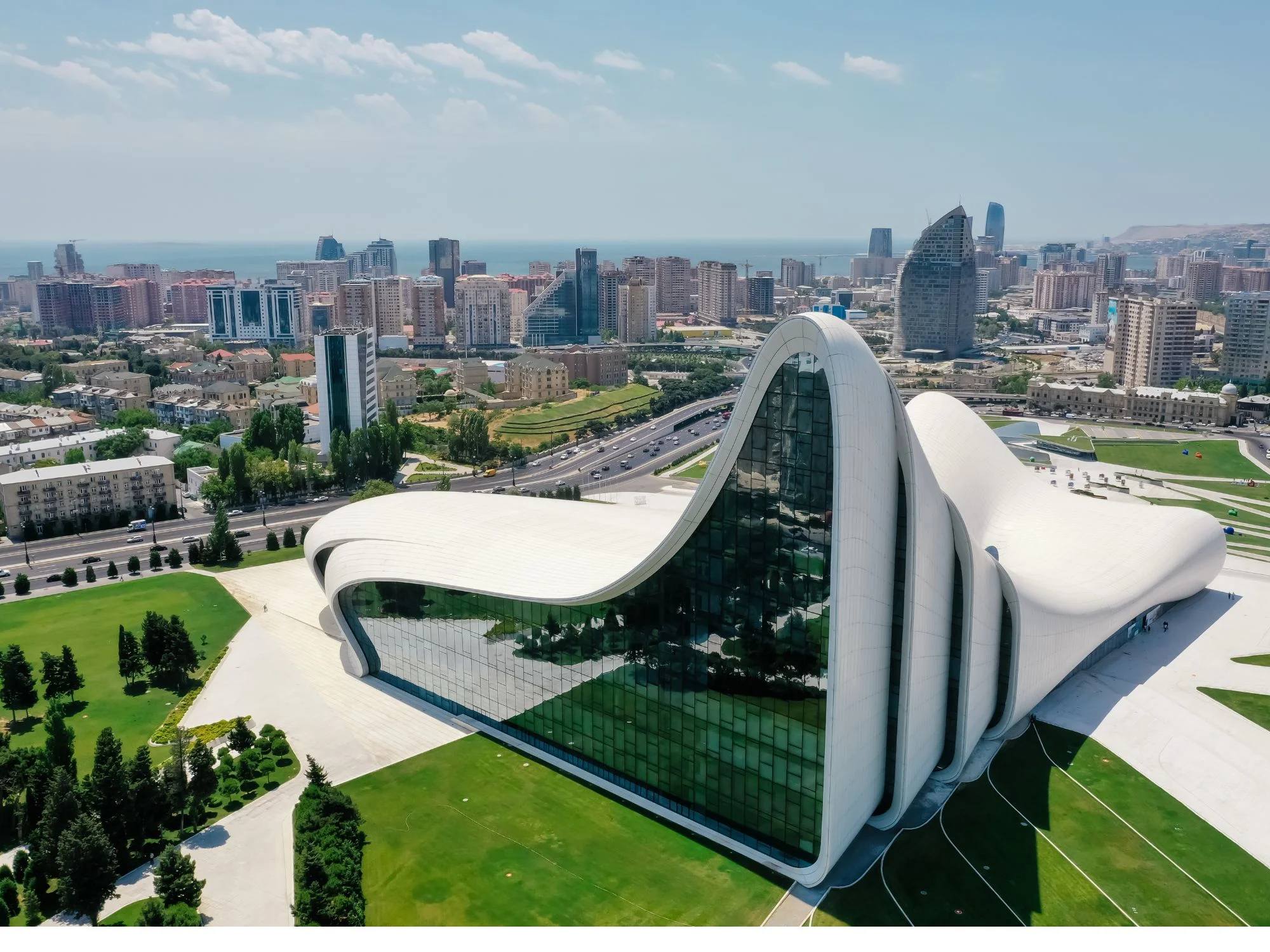 Aerial view of Baku's Heydar Aliyev Center, its sweeping white curves set in green parkland with the city skyline beyond
