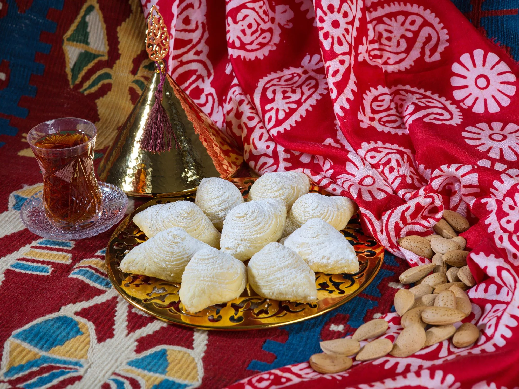 Plate of traditional Azerbaijani shekerbura sweets with armudu tea and almonds on a colourful patterned cloth
