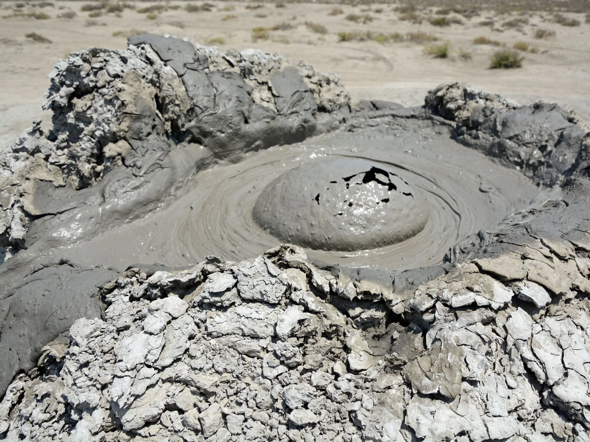 Active mud volcano in Gobustan, Azerbaijan — wet grey mud bubbling from a small crater on rugged terrain