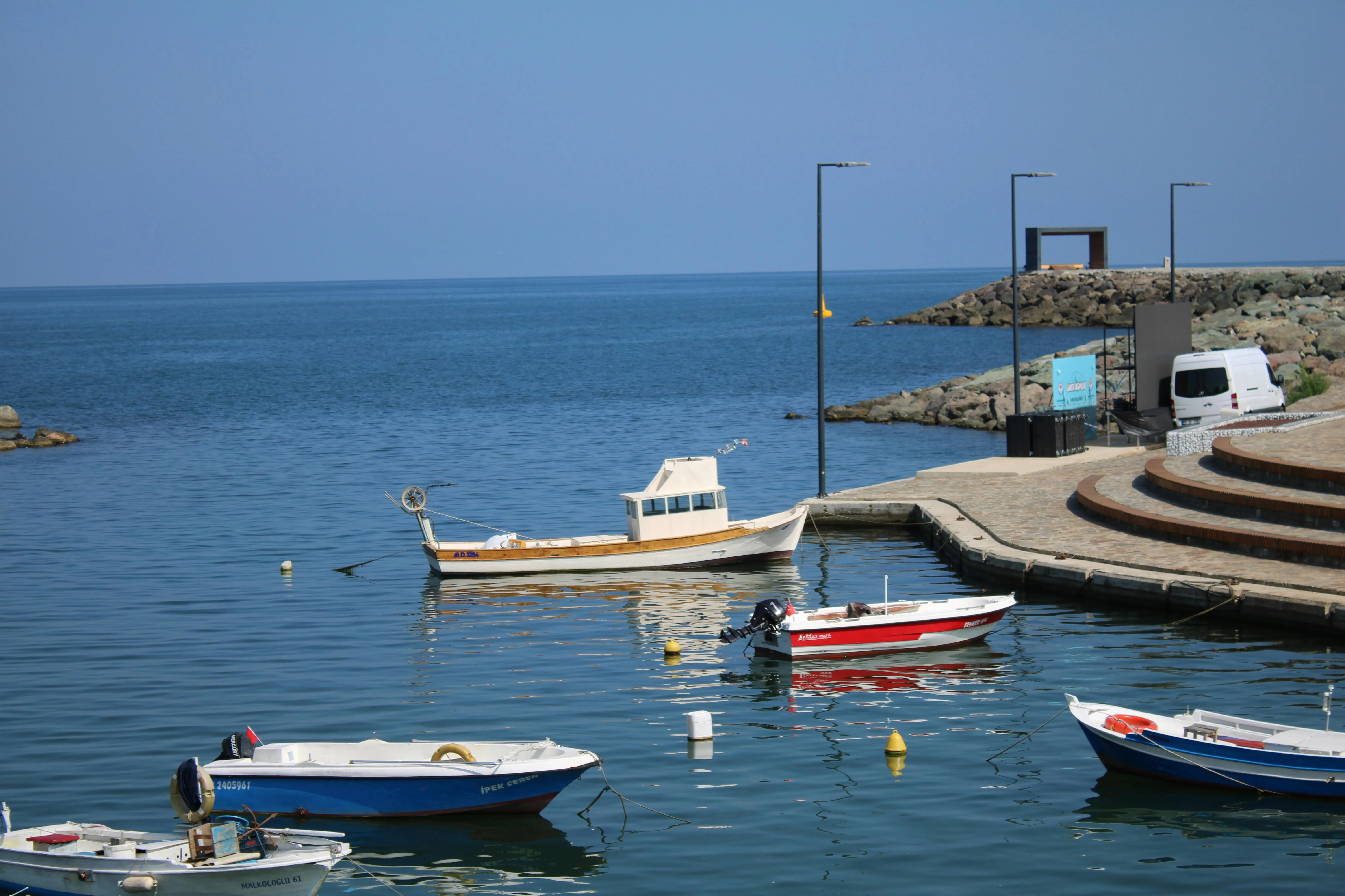 Small Black Sea fishing harbour with white wooden boats moored along a stone breakwater on a calm sunny day