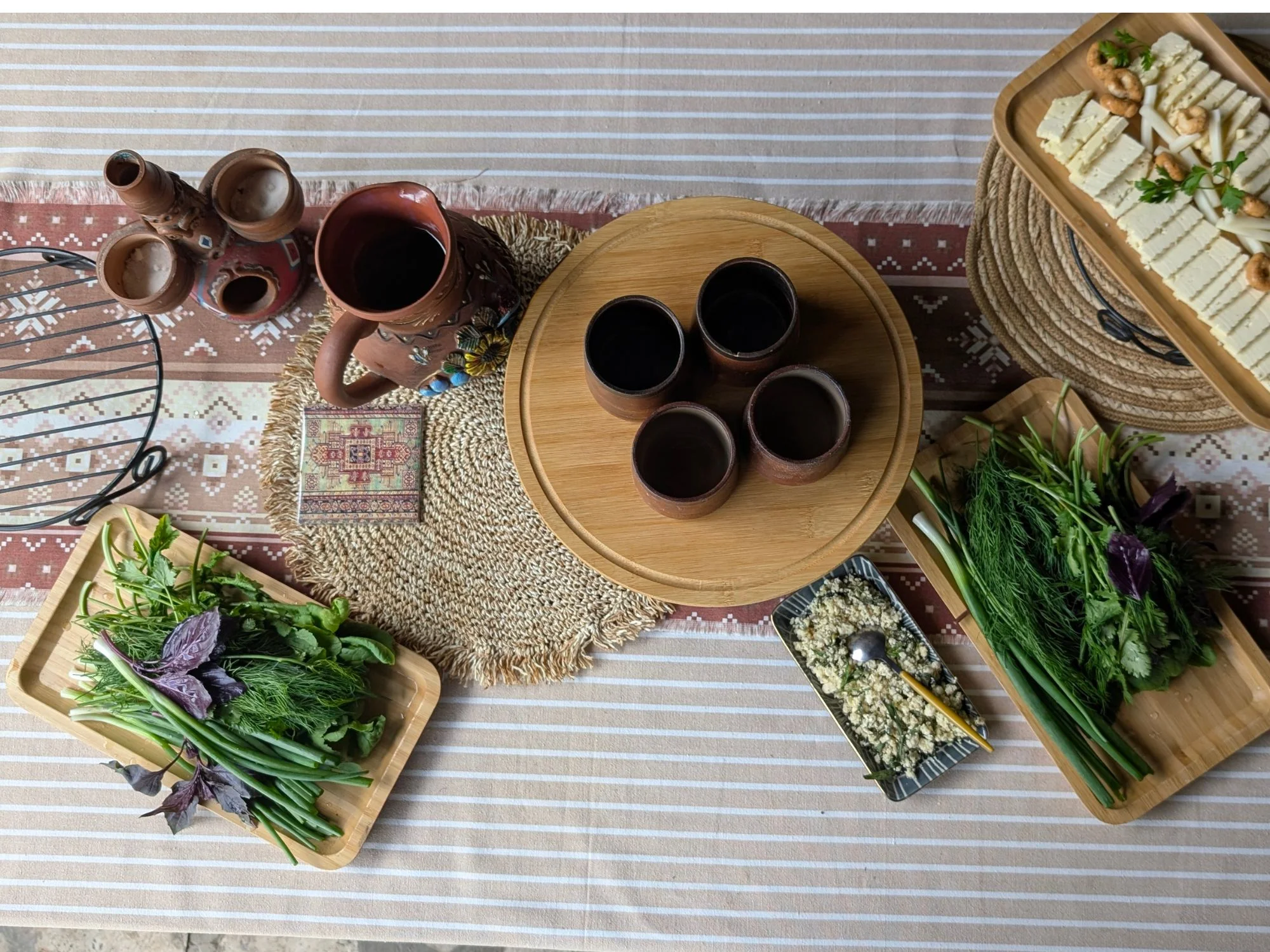 Traditional Georgian feast spread with clay wine pitcher, fresh herbs and chunks of cheese on woven textile
