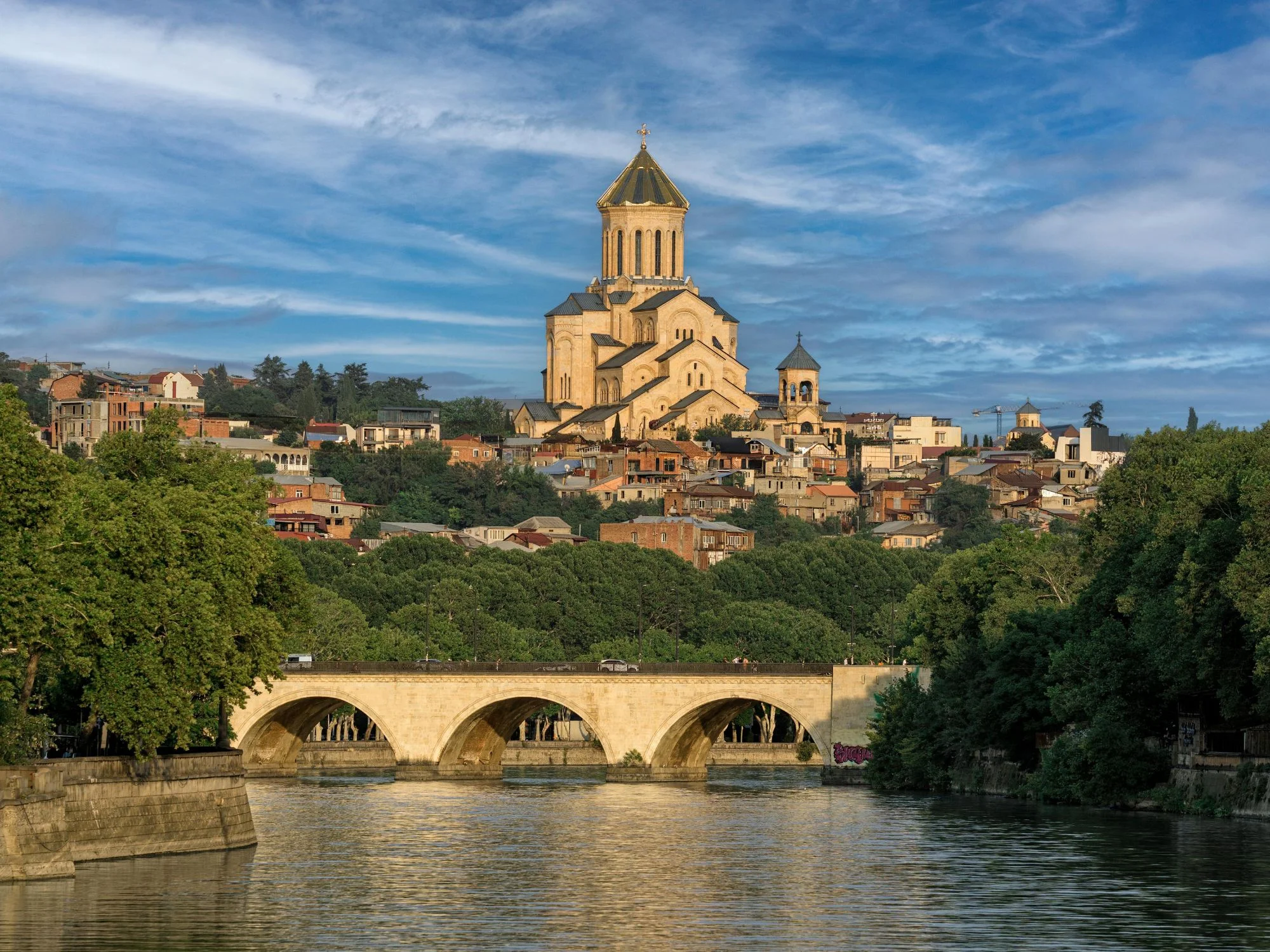 Tbilisi's Holy Trinity Cathedral (Sameba) towering above the Mtkvari River, with a stone arched bridge in front