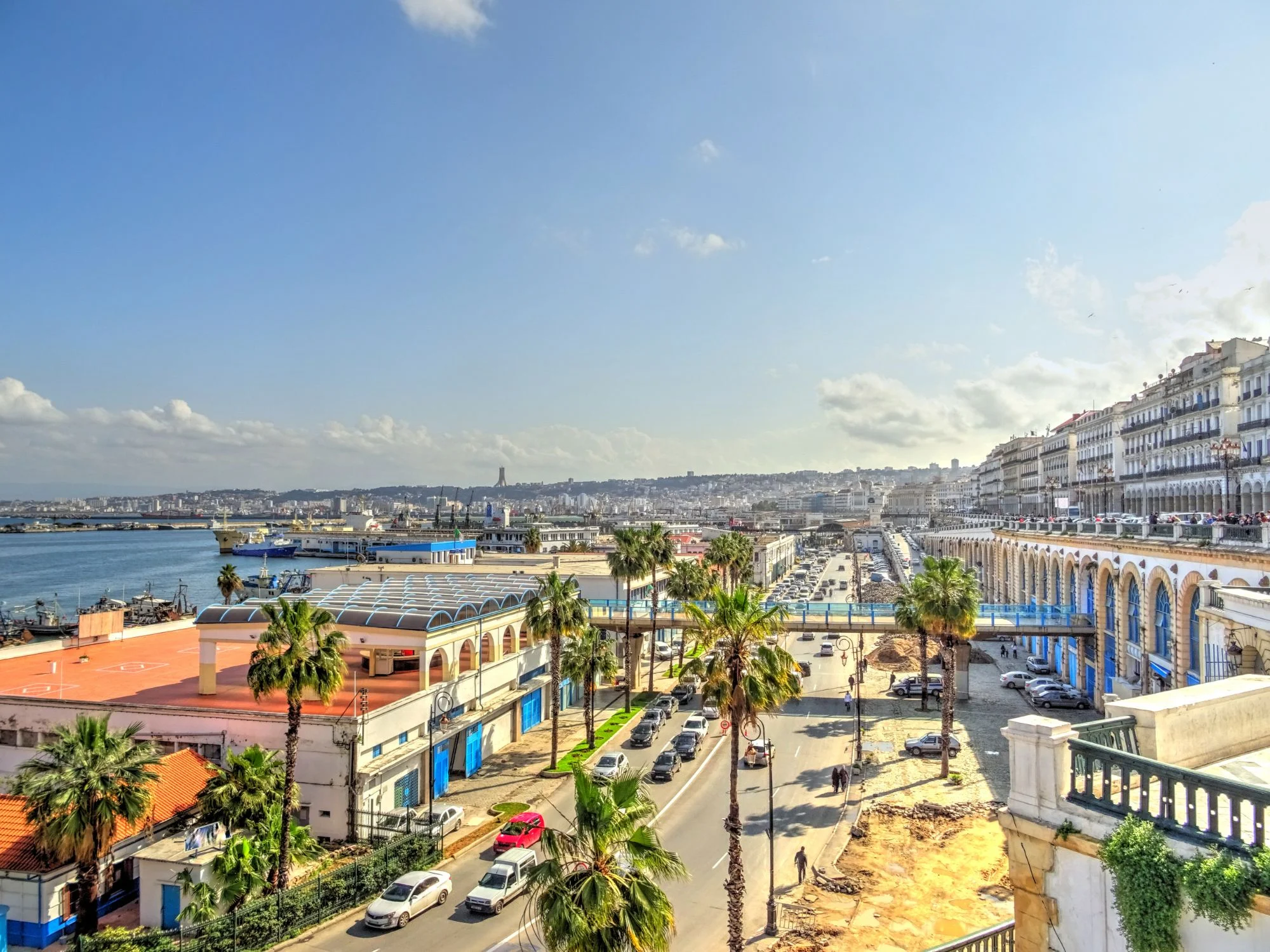 Aerial view of Algiers waterfront with palm-lined boulevards and white colonial arches above the Mediterranean harbour