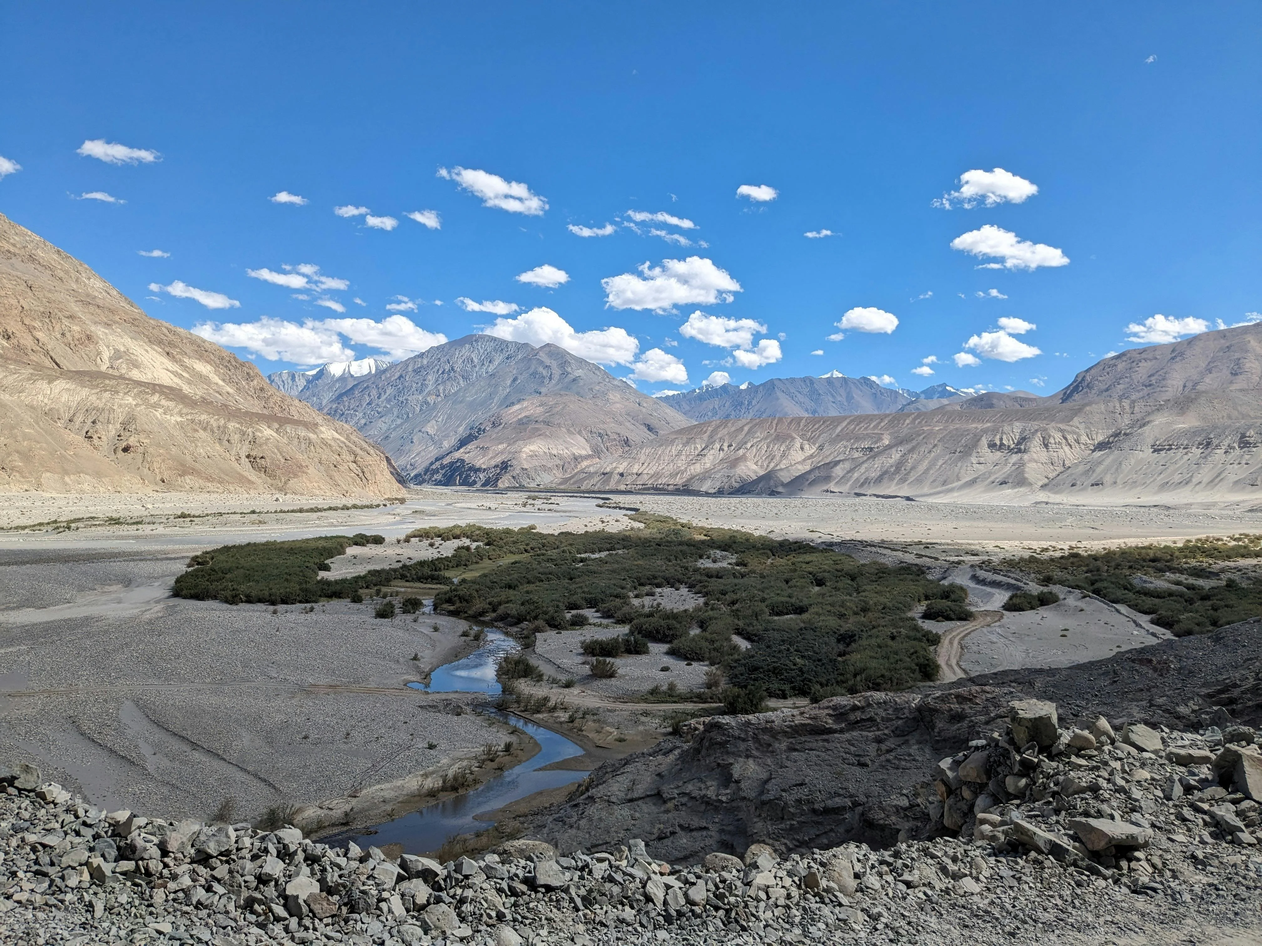 Braided river meandering through an arid high-altitude valley with rocky brown mountains and blue sky