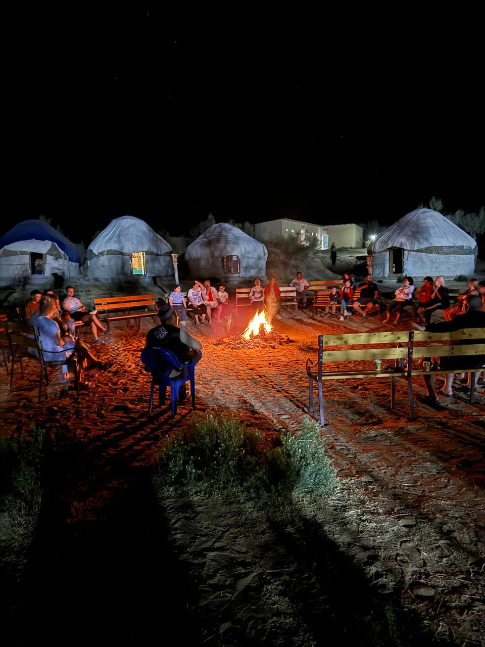 Travelers gathered around a campfire by yurts under a starry desert sky at Aydarkul, Uzbekistan