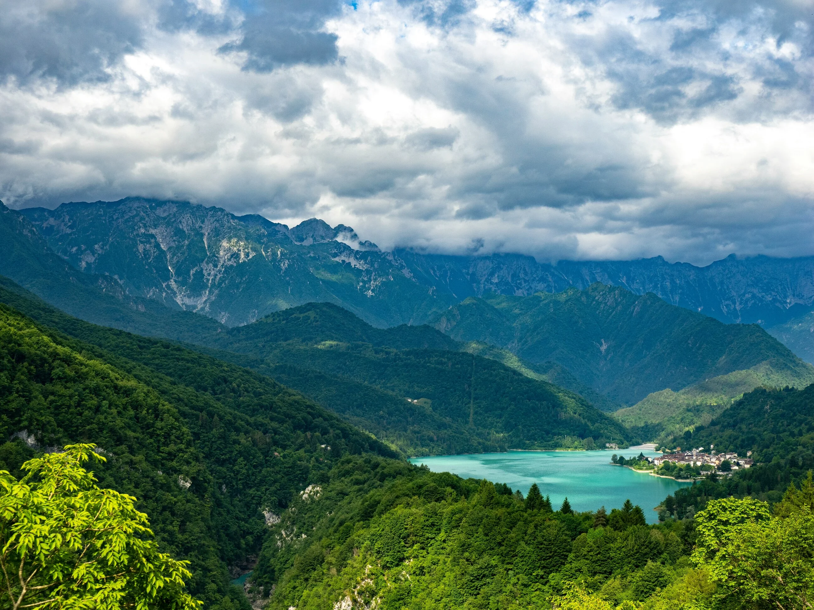 Forested valley with a turquoise lake and small village beneath jagged limestone peaks in the Dinaric Alps